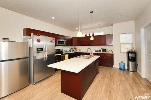 Kitchen featuring stainless steel appliances, light wood-type flooring, an island with sink, and sink