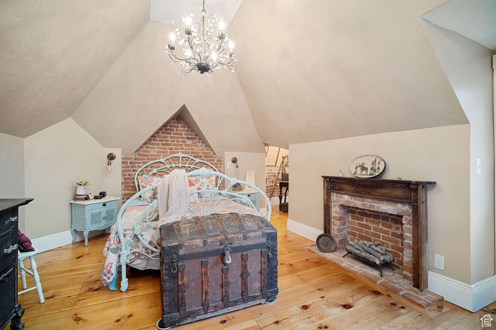 Bedroom featuring a notable chandelier, vaulted ceiling, light wood-type flooring, and brick wall