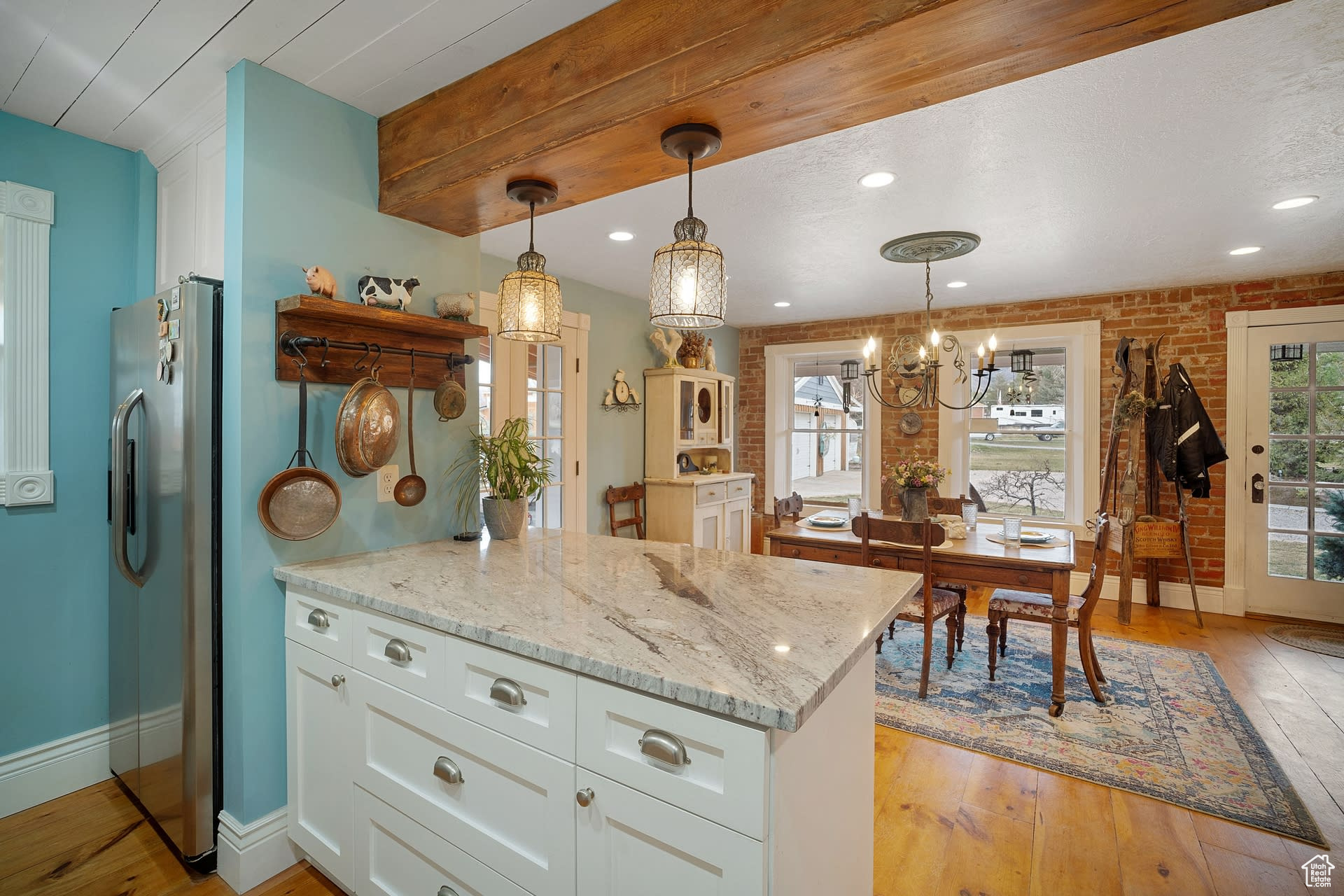 Kitchen featuring brick wall, high quality fridge, white cabinets, decorative light fixtures, and an inviting chandelier