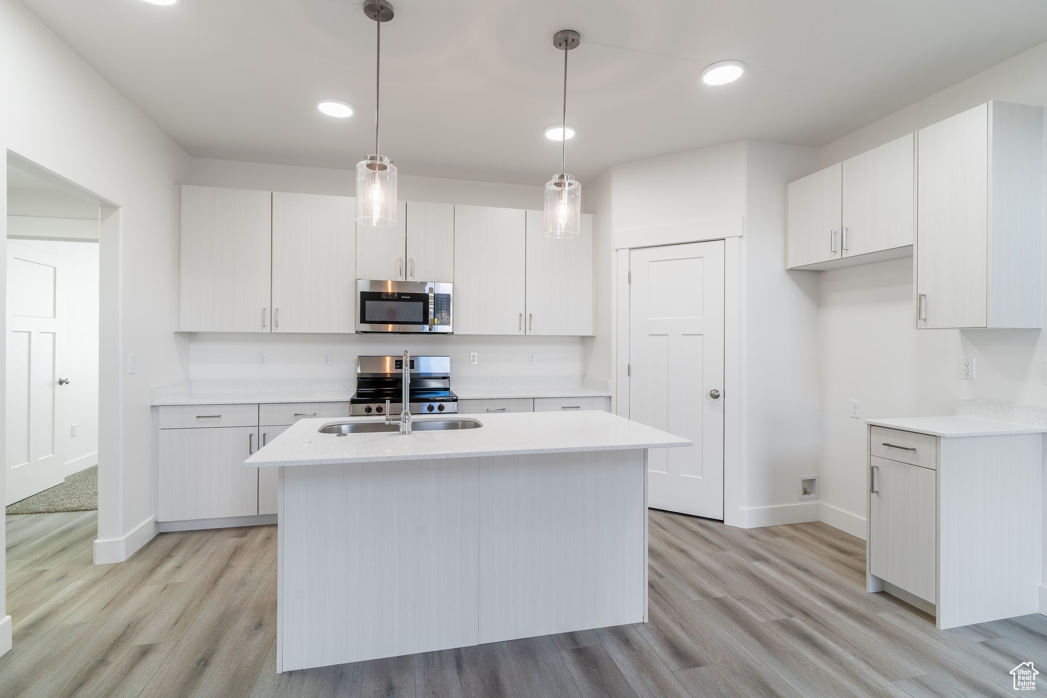 Kitchen with appliances with stainless steel finishes, white cabinetry, and a kitchen island with sink