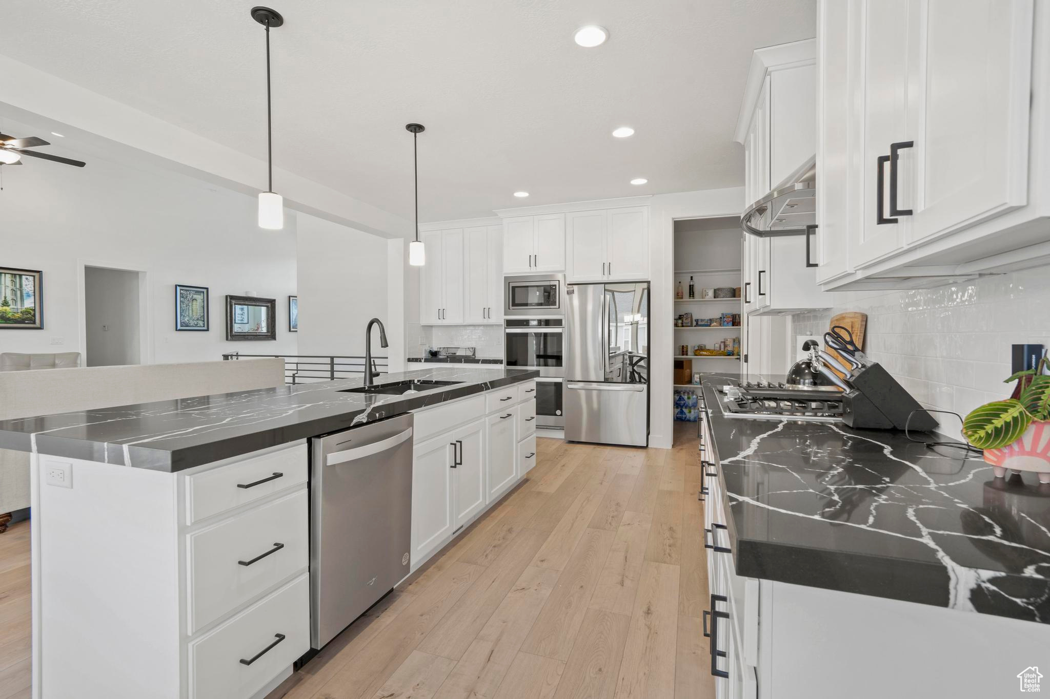 Kitchen with tasteful backsplash, appliances with stainless steel finishes, a center island with sink, white cabinets, and ceiling fan