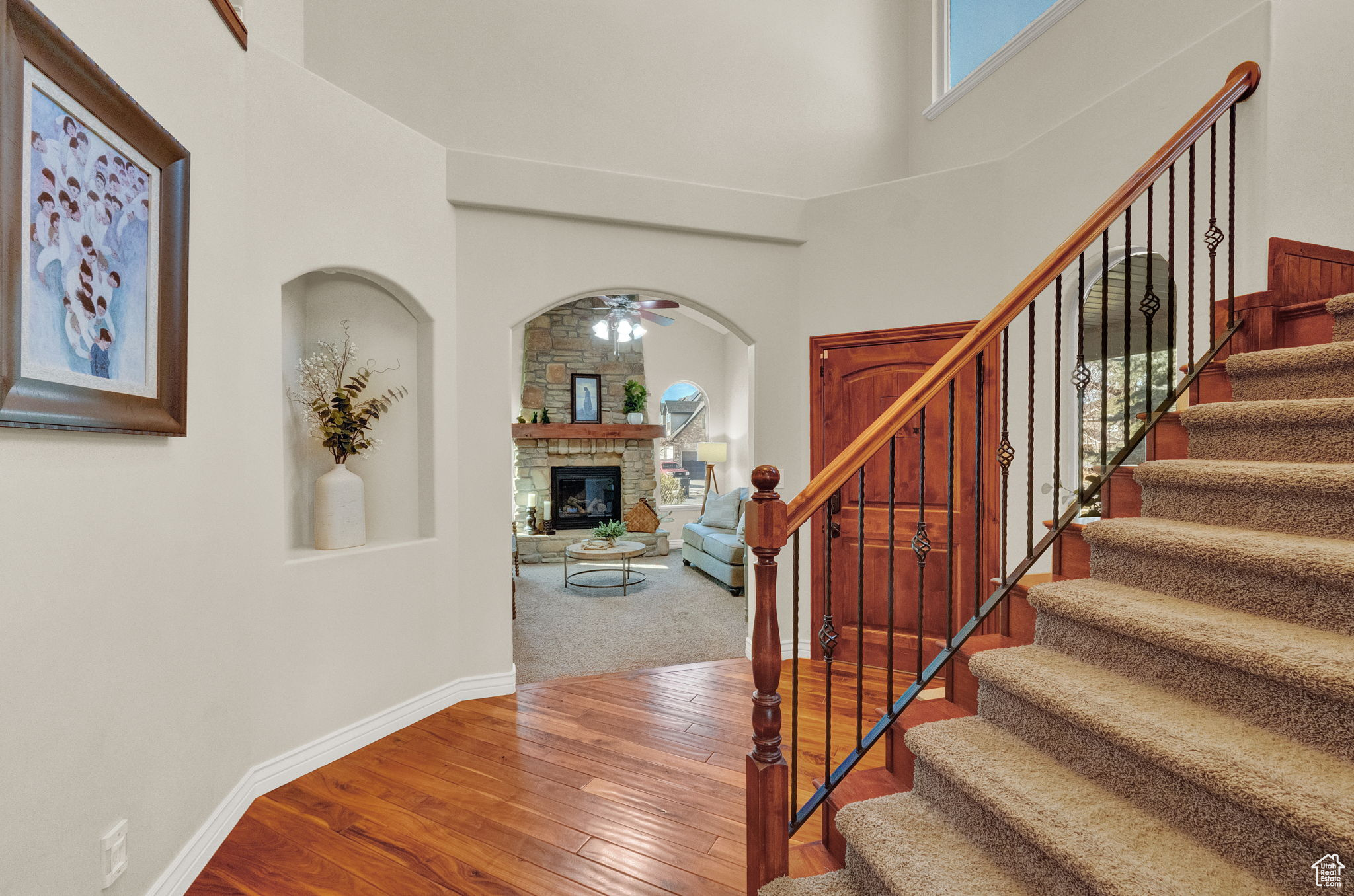 Staircase with a high ceiling, a stone fireplace, carpet flooring, and ceiling fan