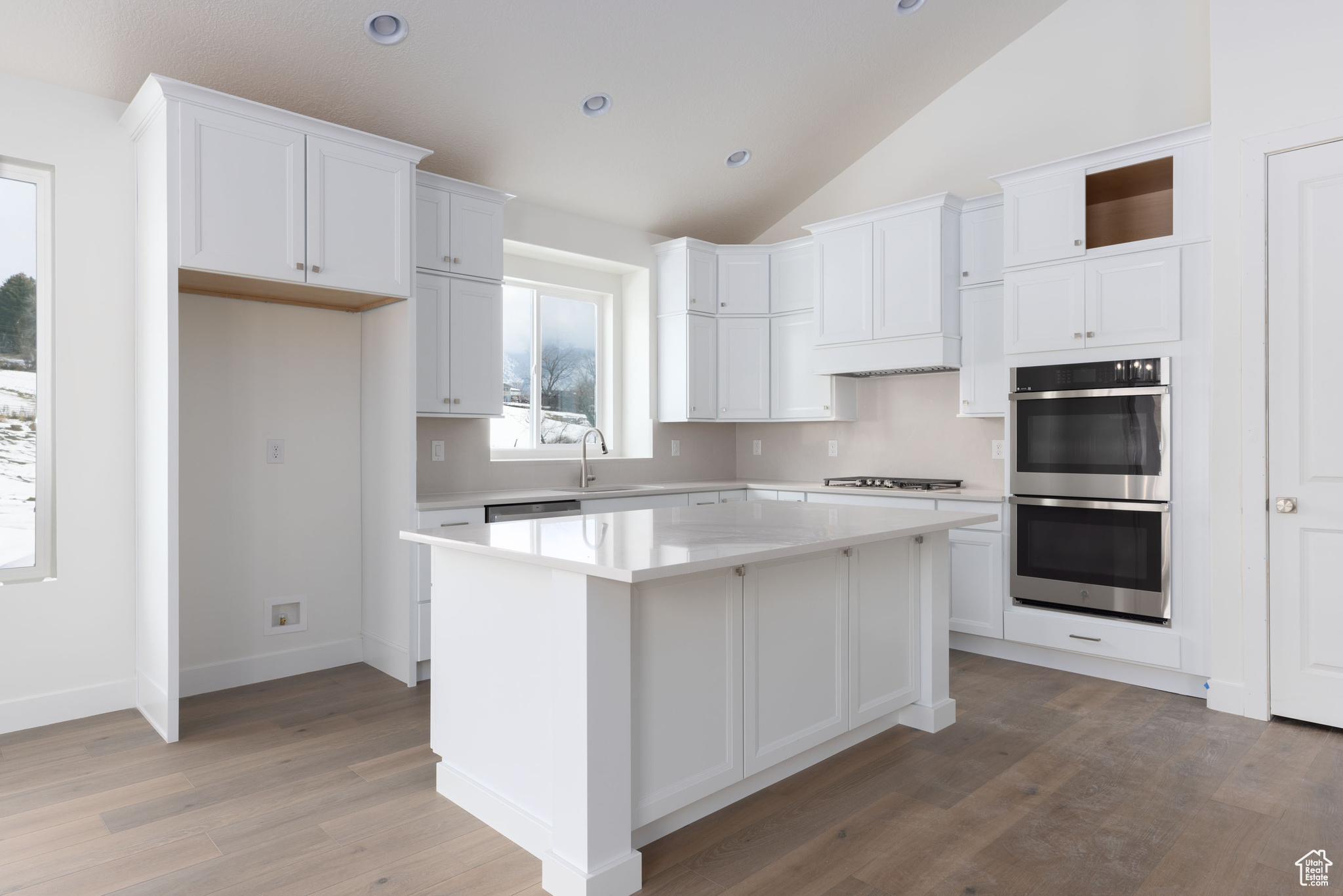 Kitchen featuring a center island, white cabinets, vaulted ceiling, light hardwood / wood-style floors, and stainless steel appliances