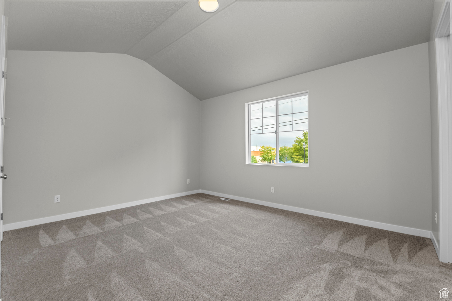 Carpeted empty room featuring vaulted ceiling