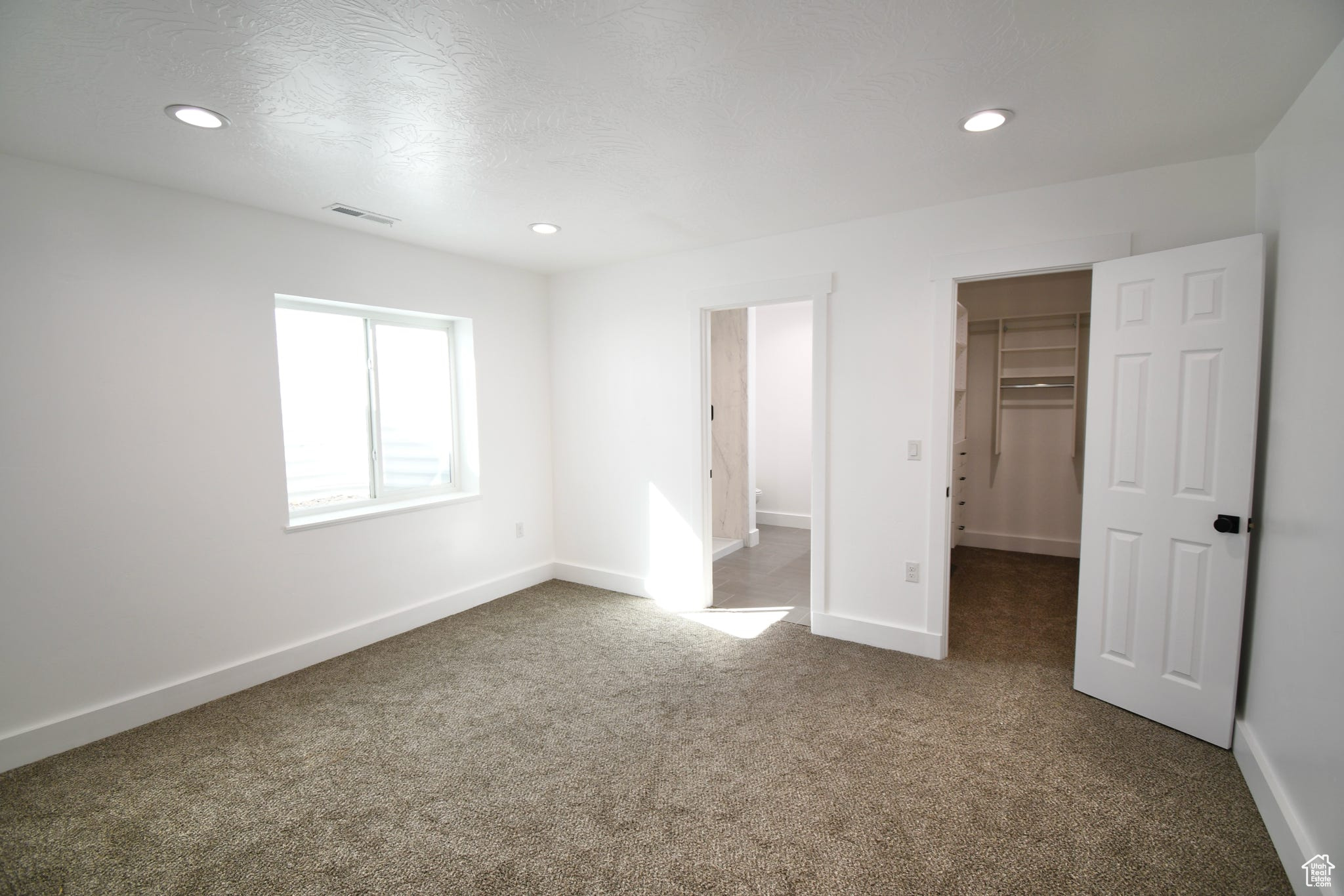 Unfurnished bedroom featuring a spacious closet, a closet, and dark carpet