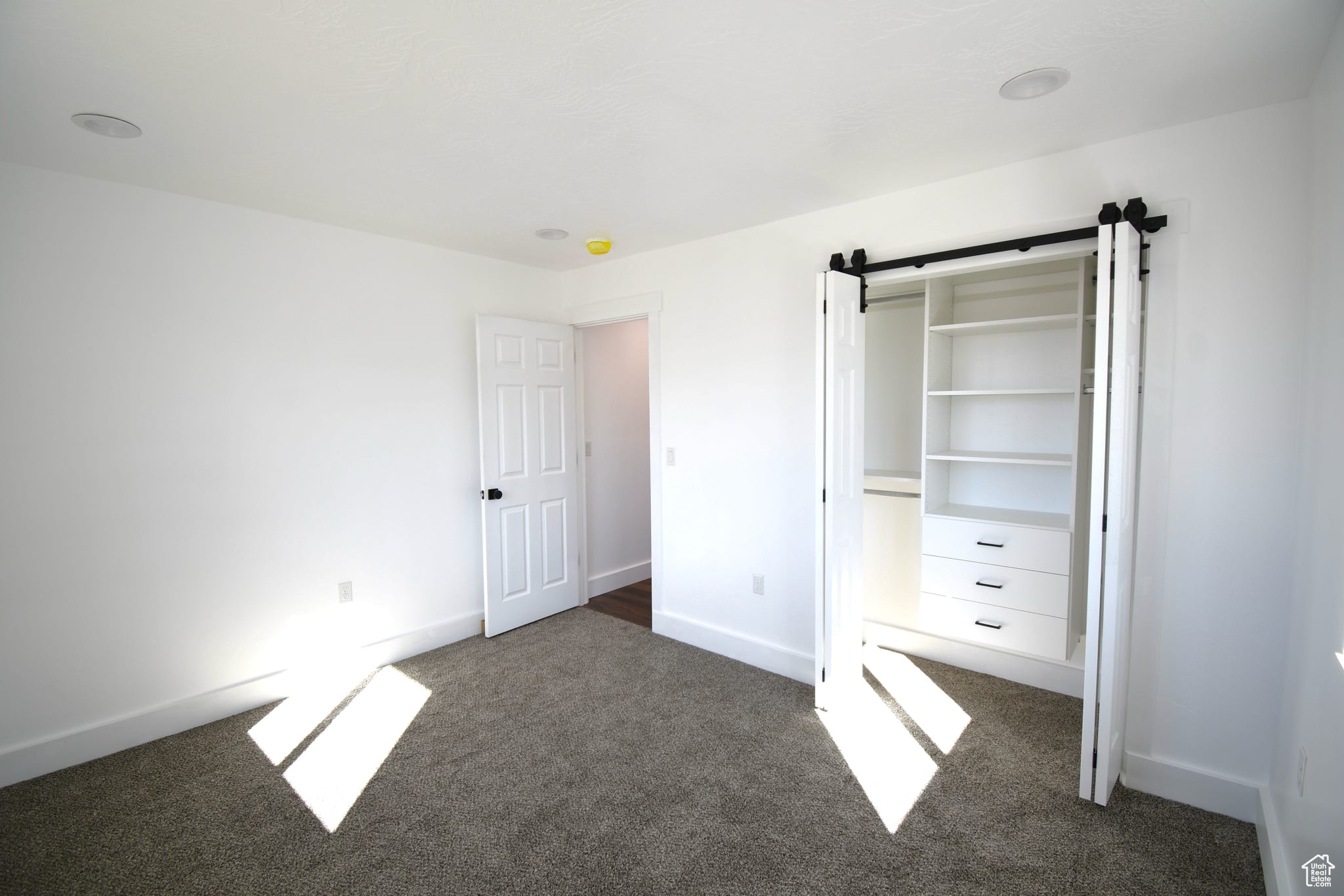 Unfurnished bedroom with a barn door and dark colored carpet