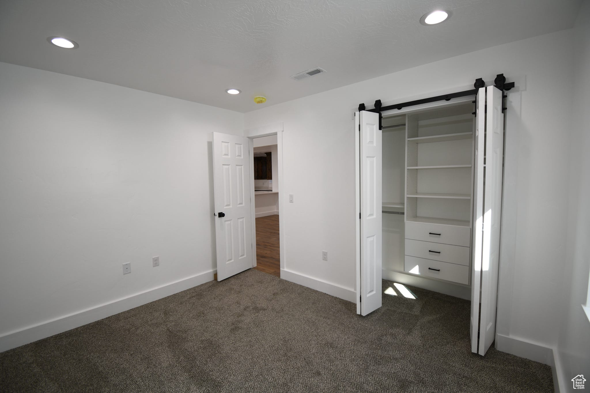 Unfurnished bedroom featuring dark colored carpet, a barn door, and a closet