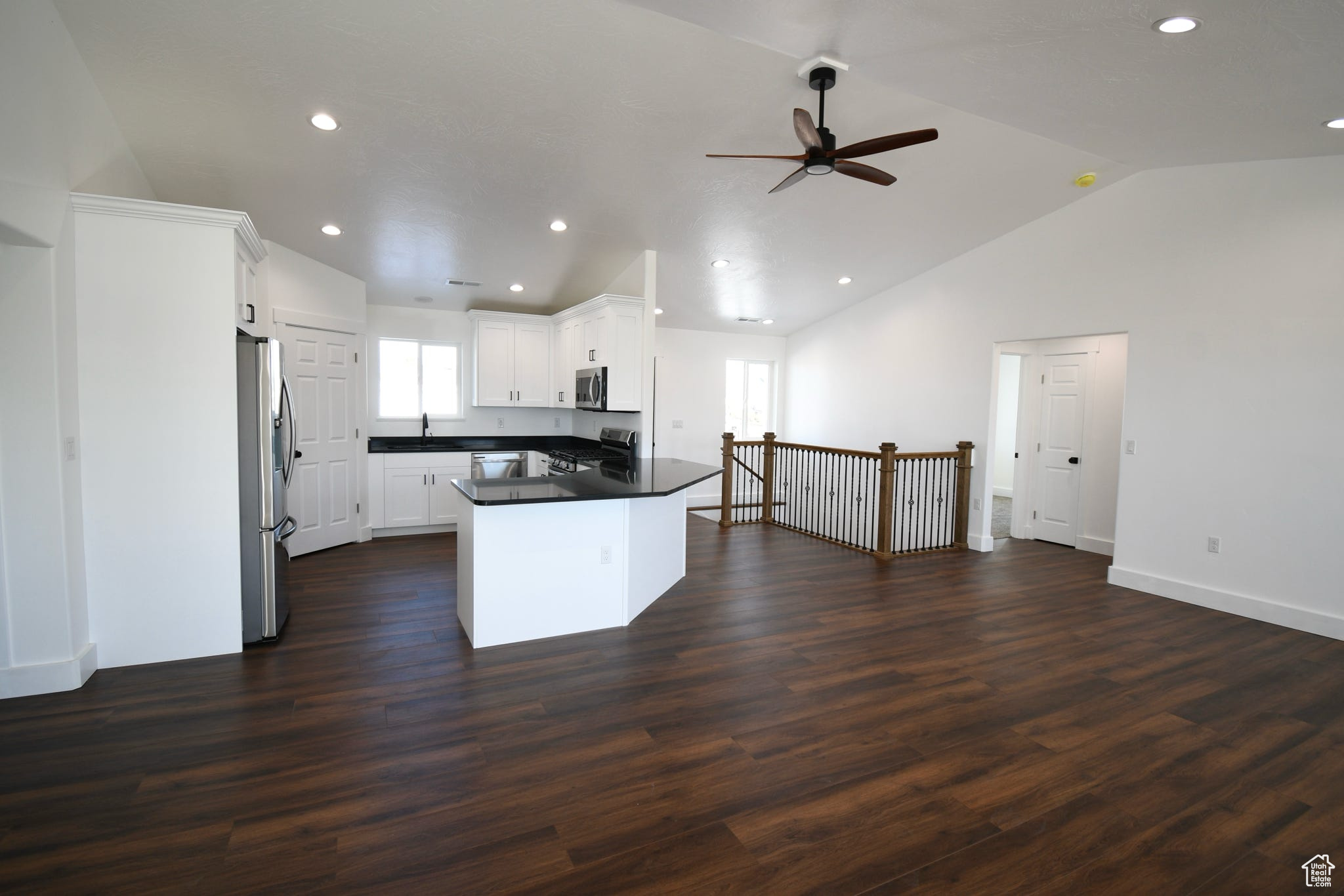 Kitchen with lofted ceiling, ceiling fan, dark wood-type flooring, white cabinetry, and stainless steel appliances