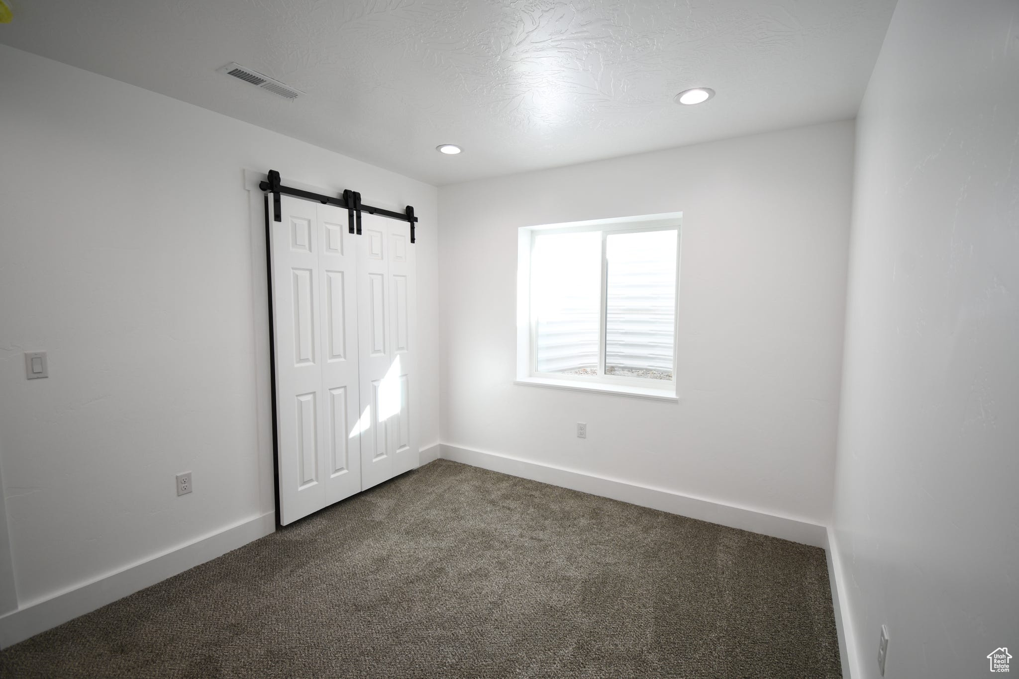 Unfurnished bedroom featuring dark colored carpet, a closet, and a barn door