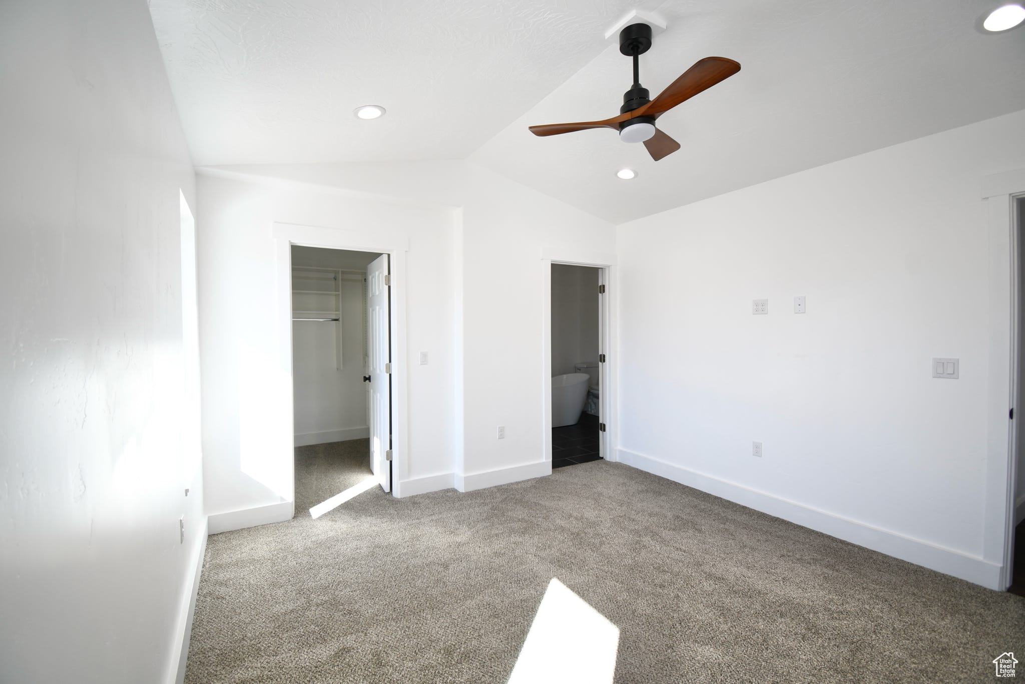Unfurnished bedroom with connected bathroom, light colored carpet, lofted ceiling, a closet, and ceiling fan