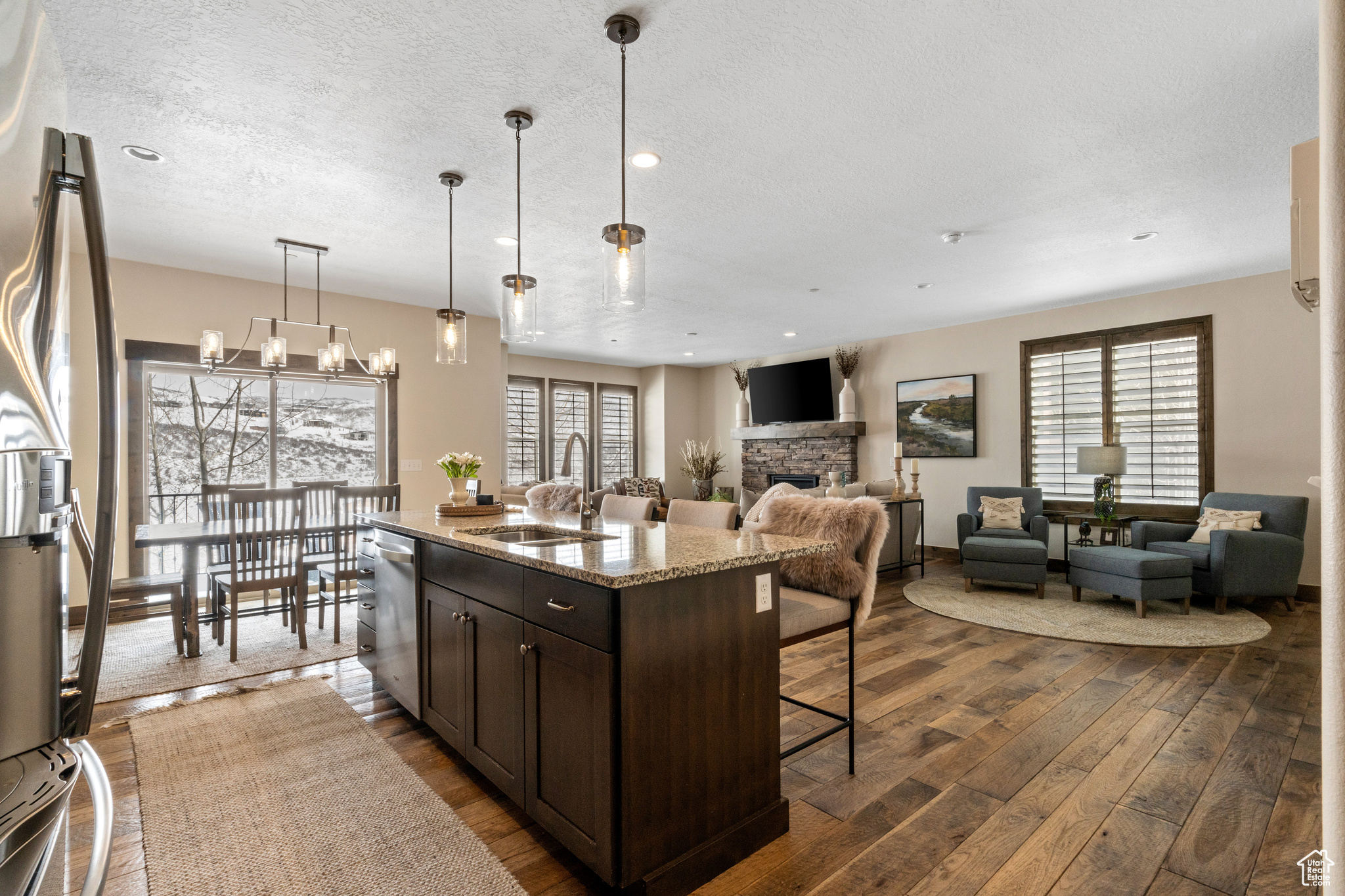 Kitchen with decorative light fixtures, dark wood-type flooring, sink, a stone fireplace, and light stone countertops