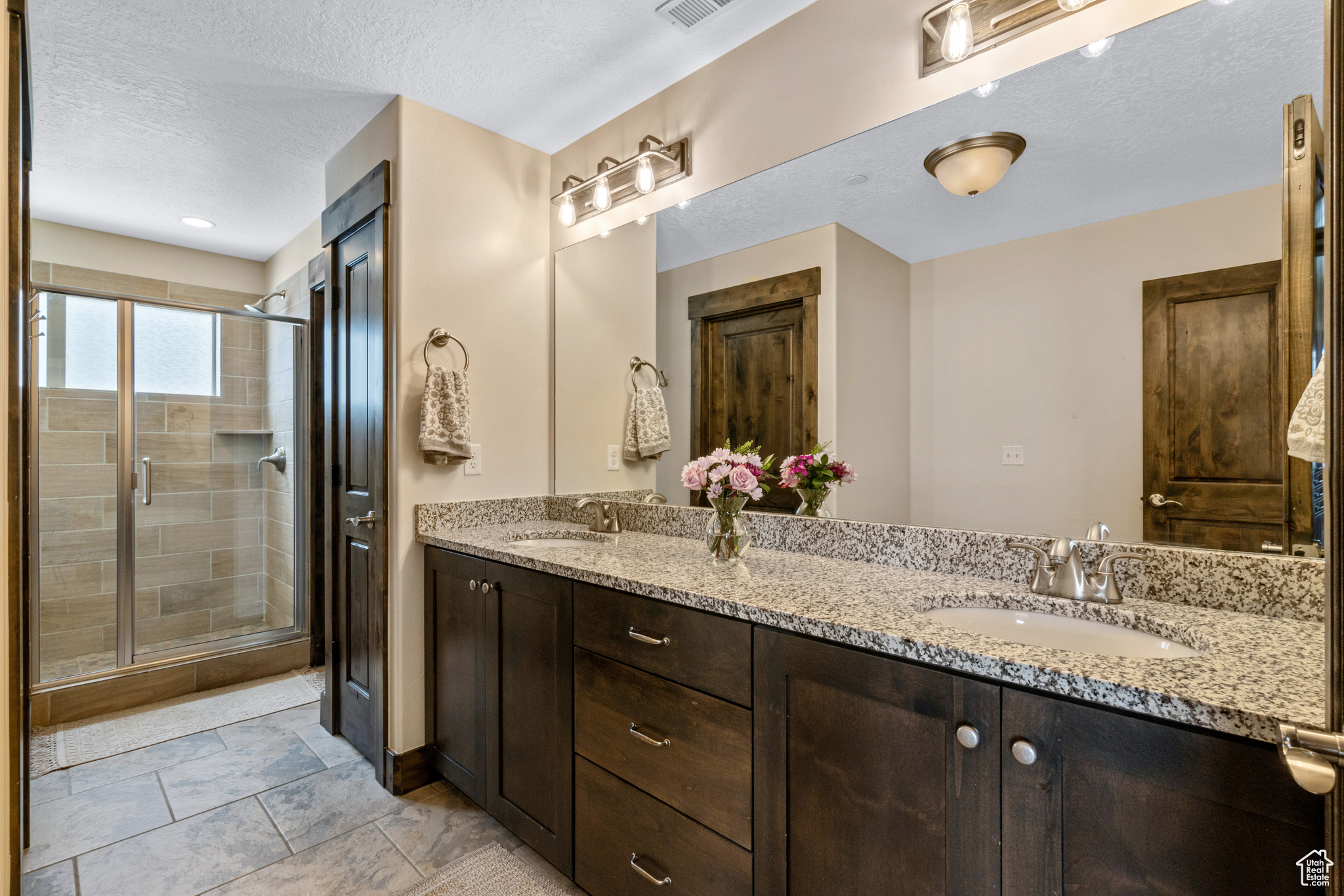 Bathroom featuring a textured ceiling, a shower with shower door, oversized vanity, tile flooring, and double sink