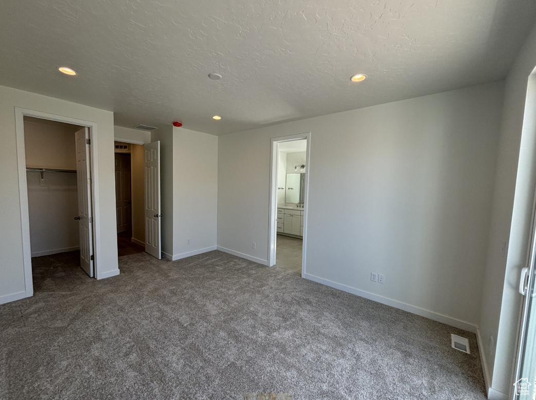Unfurnished bedroom with a closet, carpet floors, ensuite bath, a spacious closet, and a textured ceiling