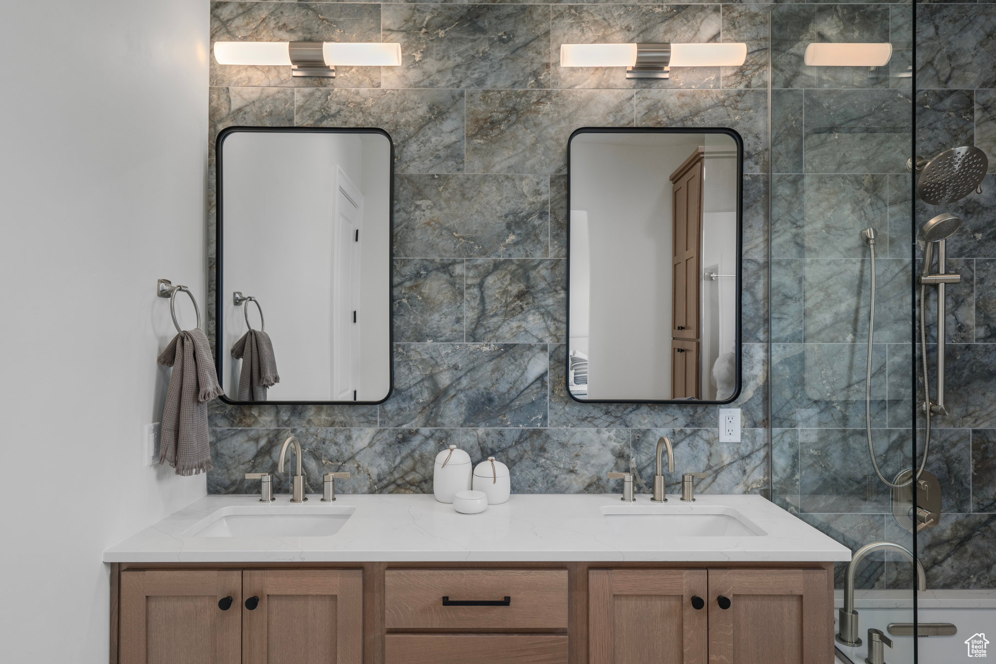 Bathroom with double sink, vanity with extensive cabinet space, tile walls, and a shower with shower door