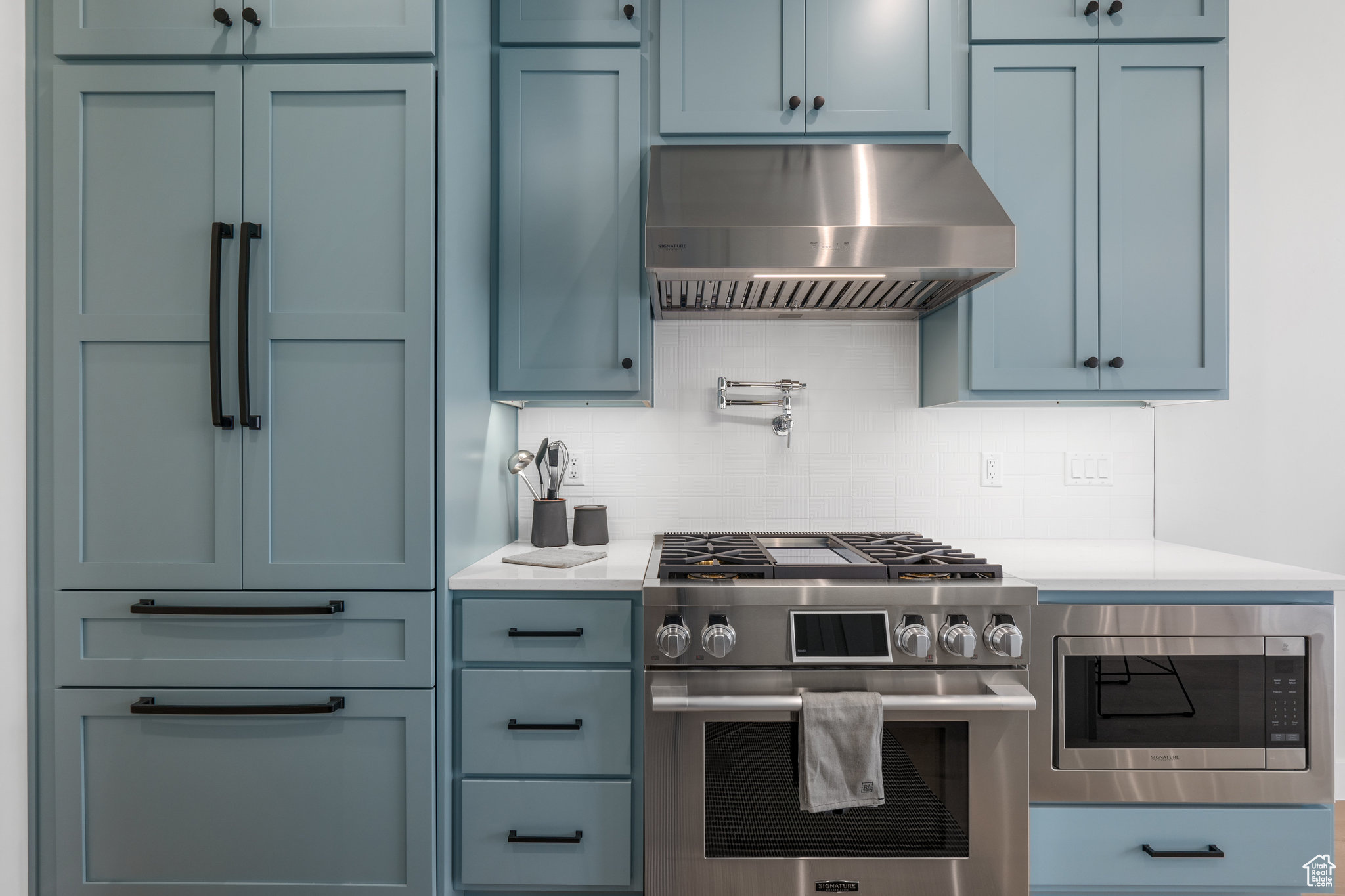 Kitchen featuring wall chimney exhaust hood, built in appliances, and tasteful backsplash