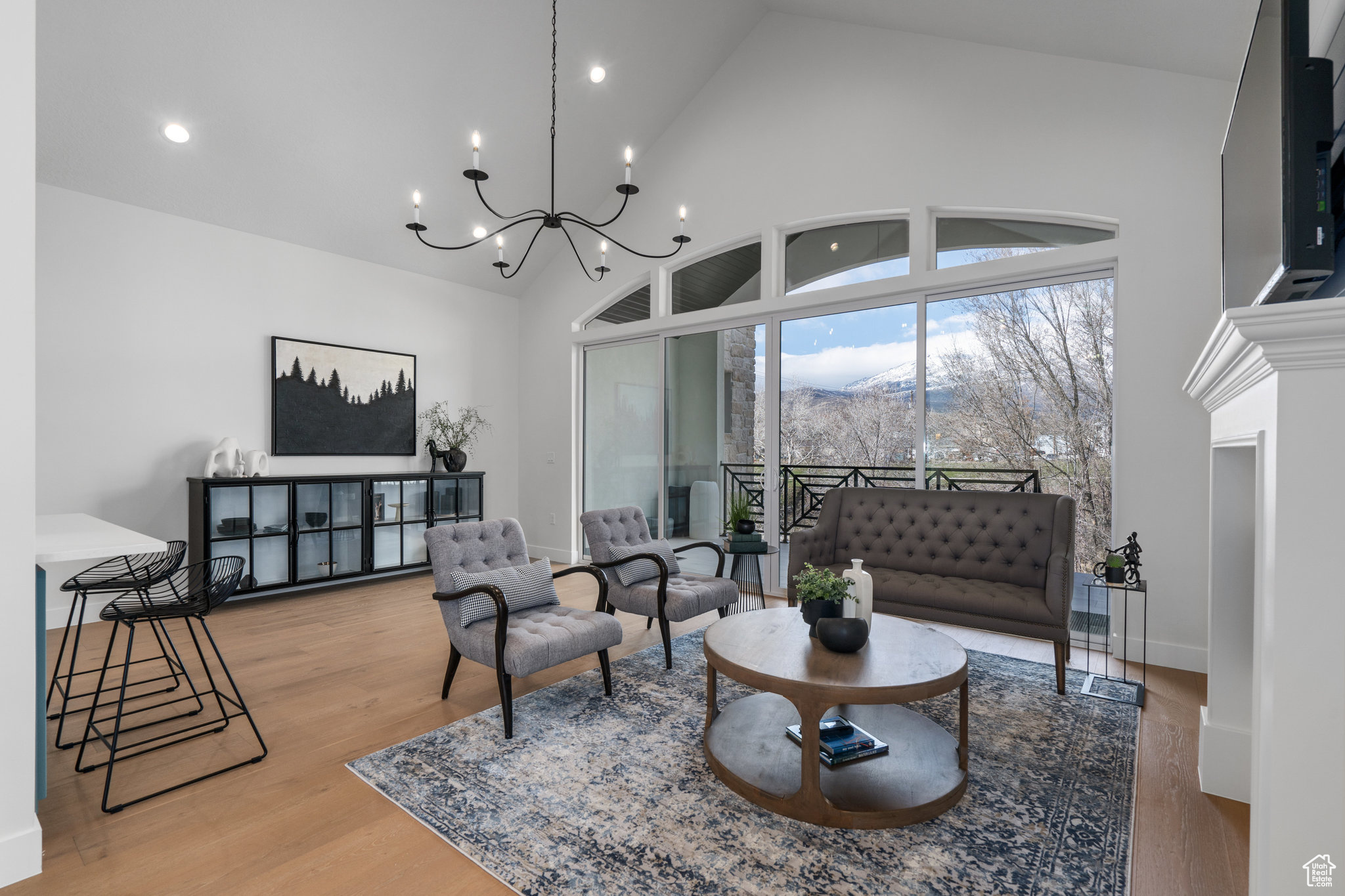 Living room with an inviting chandelier, light hardwood / wood-style flooring, a fireplace, and high vaulted ceiling