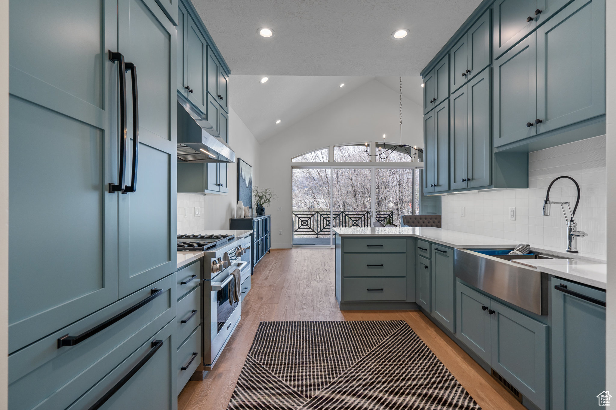 Kitchen with light wood-type flooring, stainless steel appliances, lofted ceiling, and tasteful backsplash