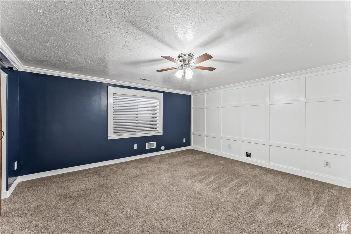 Basement bedroom with carpet, crown molding, a textured ceiling, and ceiling fan