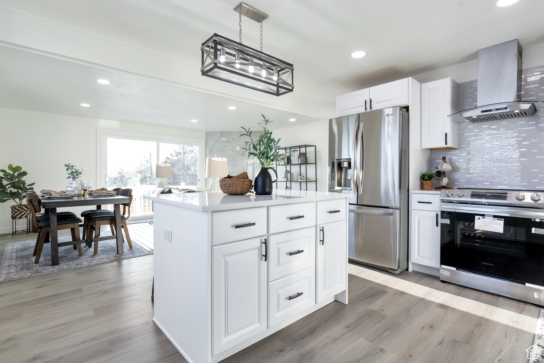 Kitchen featuring decorative light fixtures, wall chimney exhaust hood, backsplash, appliances with stainless steel finishes, and light hardwood / wood-style flooring
