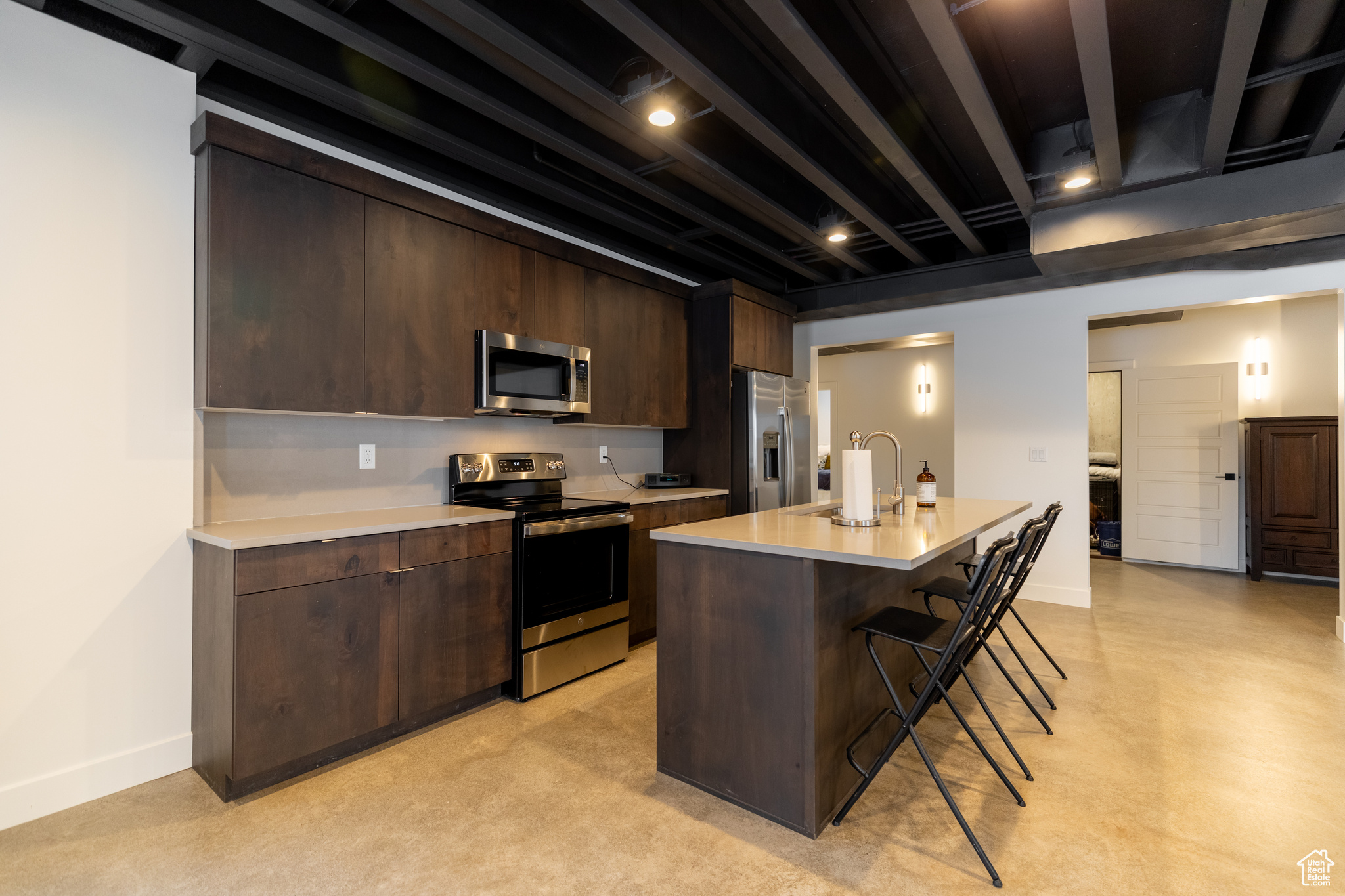 Kitchen with a center island with sink, stainless steel appliances, sink, a breakfast bar area, and dark brown cabinets