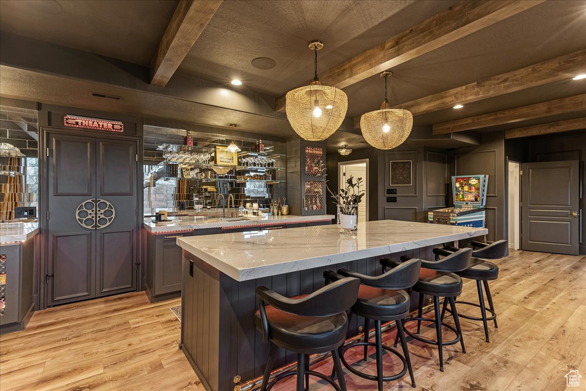 Bar with beam ceiling, light stone countertops, decorative light fixtures, light hardwood / wood-style floors, and dark brown cabinetry