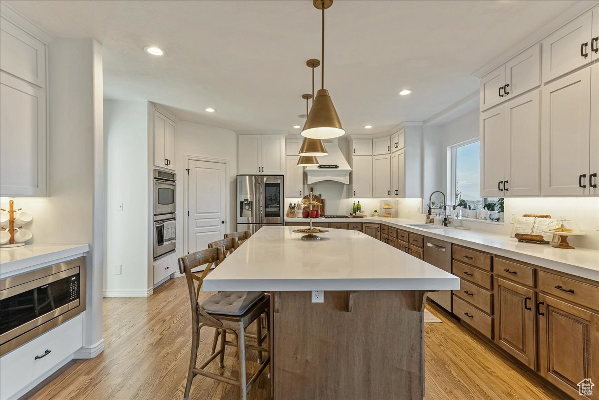 Kitchen featuring a kitchen island, light hardwood / wood-style flooring, white cabinets, and stainless steel appliances