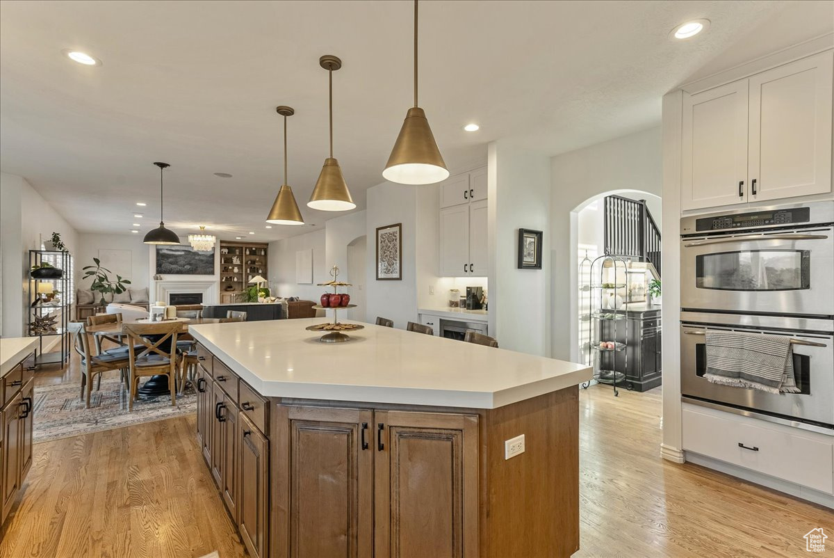 Kitchen with a kitchen island, light hardwood / wood-style flooring, white cabinets, and stainless steel double oven