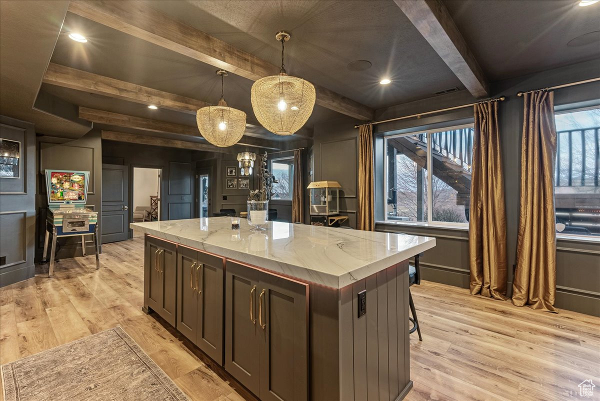 Kitchen with a kitchen island, decorative light fixtures, light hardwood / wood-style floors, and light stone countertops