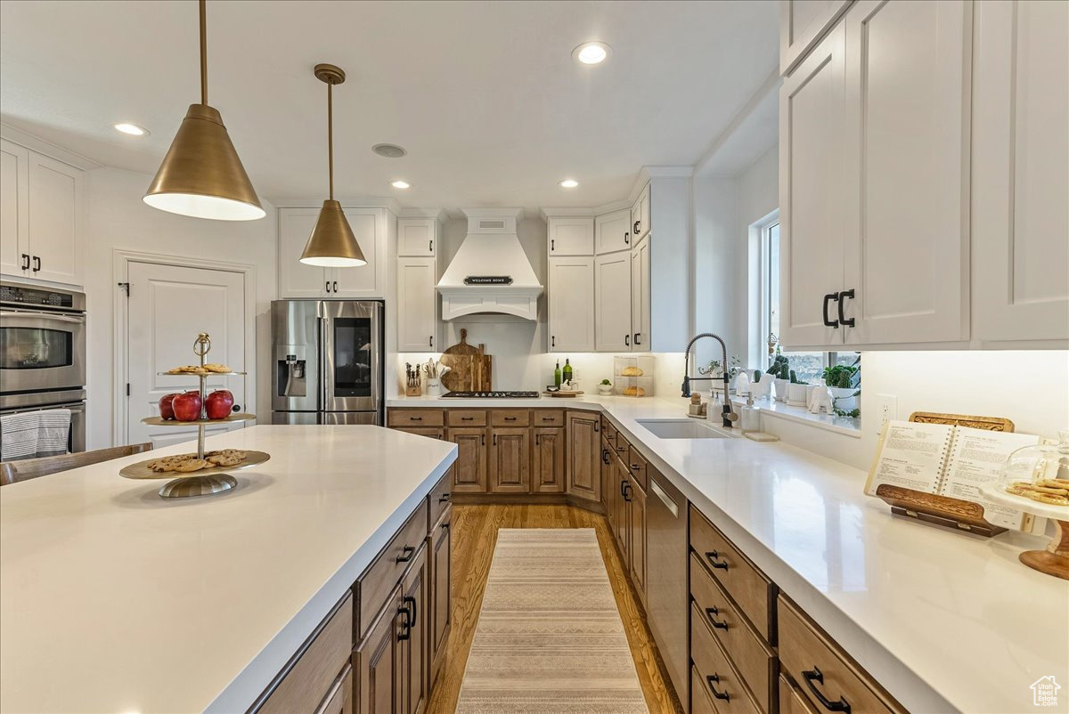 Kitchen featuring custom range hood, appliances with stainless steel finishes, white cabinetry, sink, and hanging light fixtures