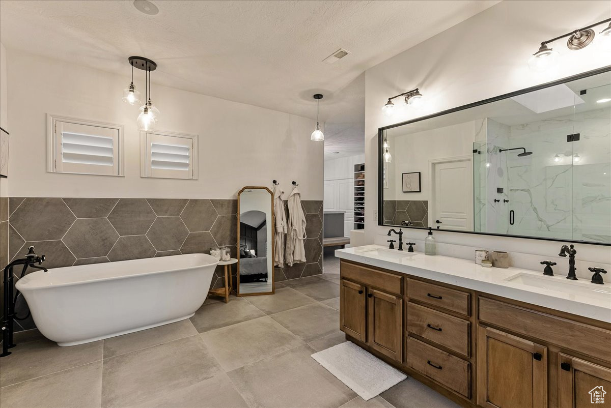 Bathroom with tile flooring, separate shower and tub, tile walls, and dual vanity