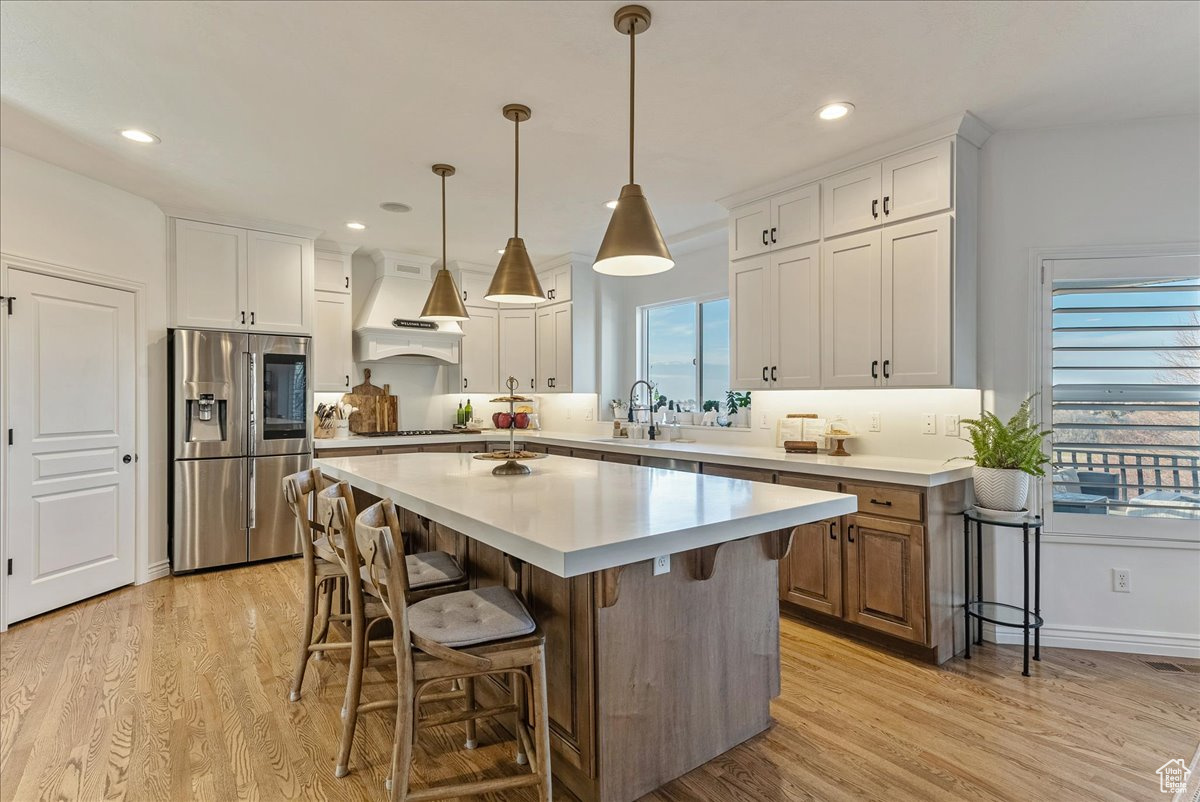 Kitchen with custom range hood, stainless steel fridge, a center island, light hardwood / wood-style floors, and white cabinetry