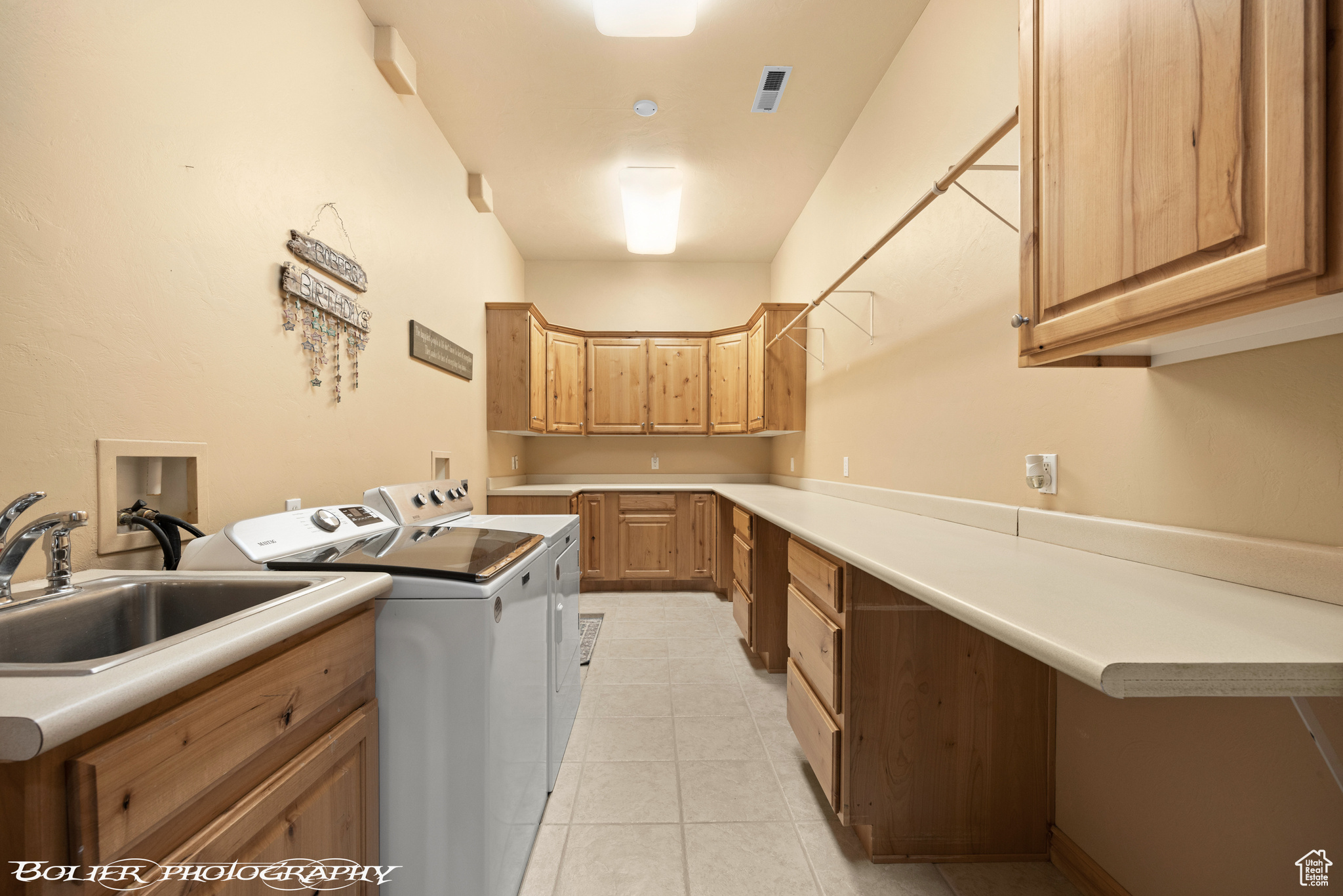 Clothes washing area featuring light tile flooring, cabinets, sink, washer and clothes dryer, and hookup for a washing machine