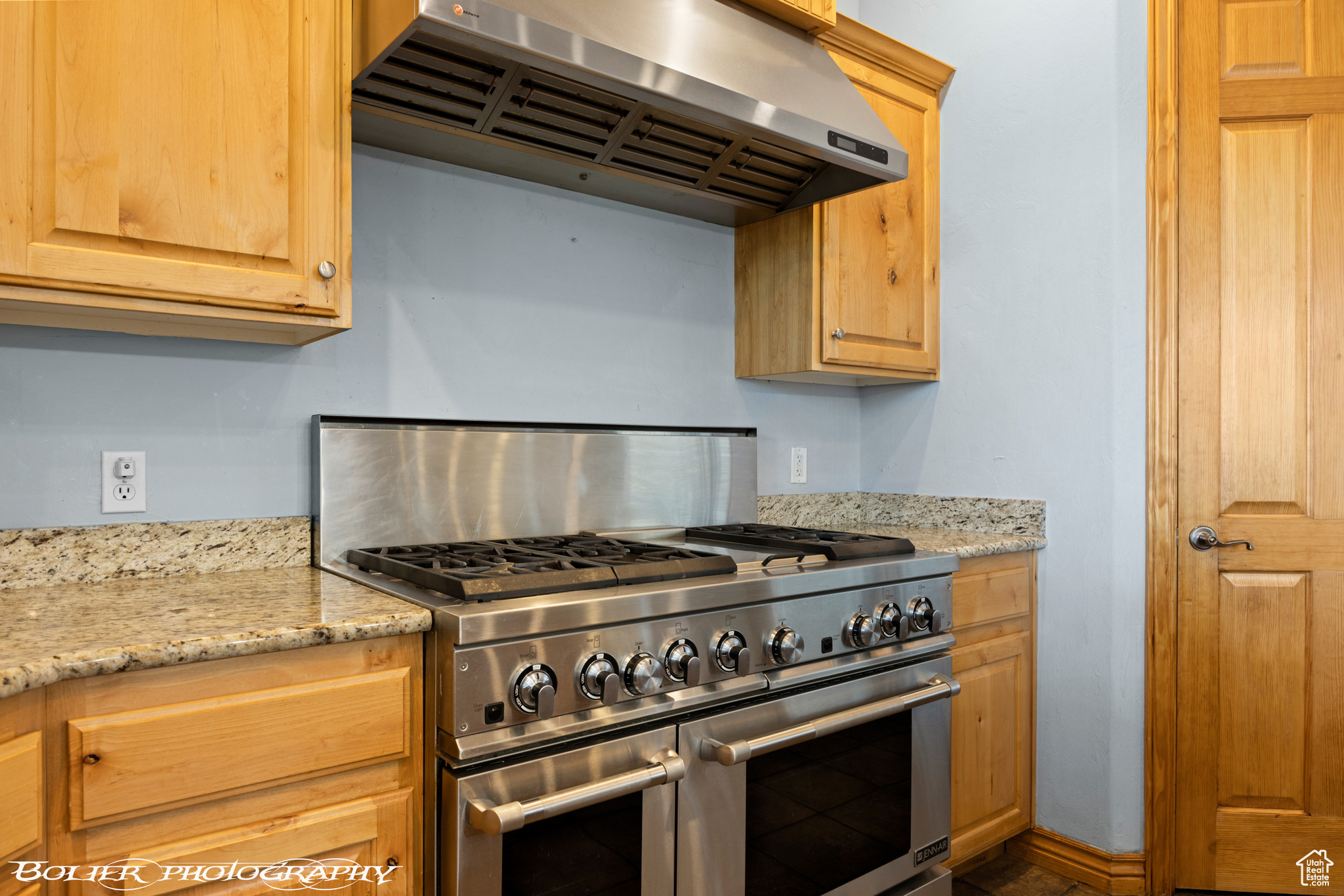 Kitchen featuring extractor fan, light stone countertops, and range with two ovens