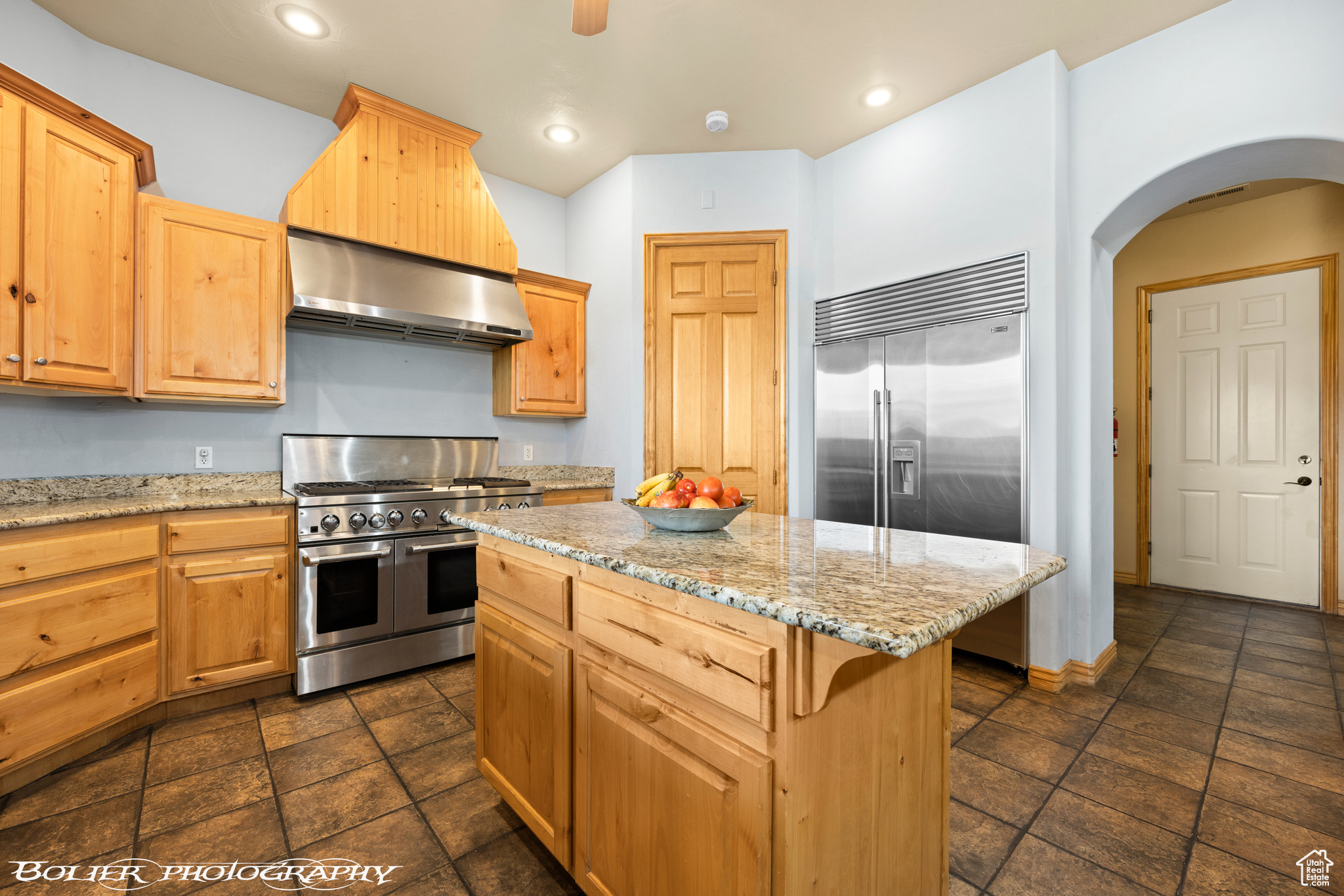 Kitchen with a kitchen island, premium appliances, light stone counters, wall chimney range hood, and dark tile floors