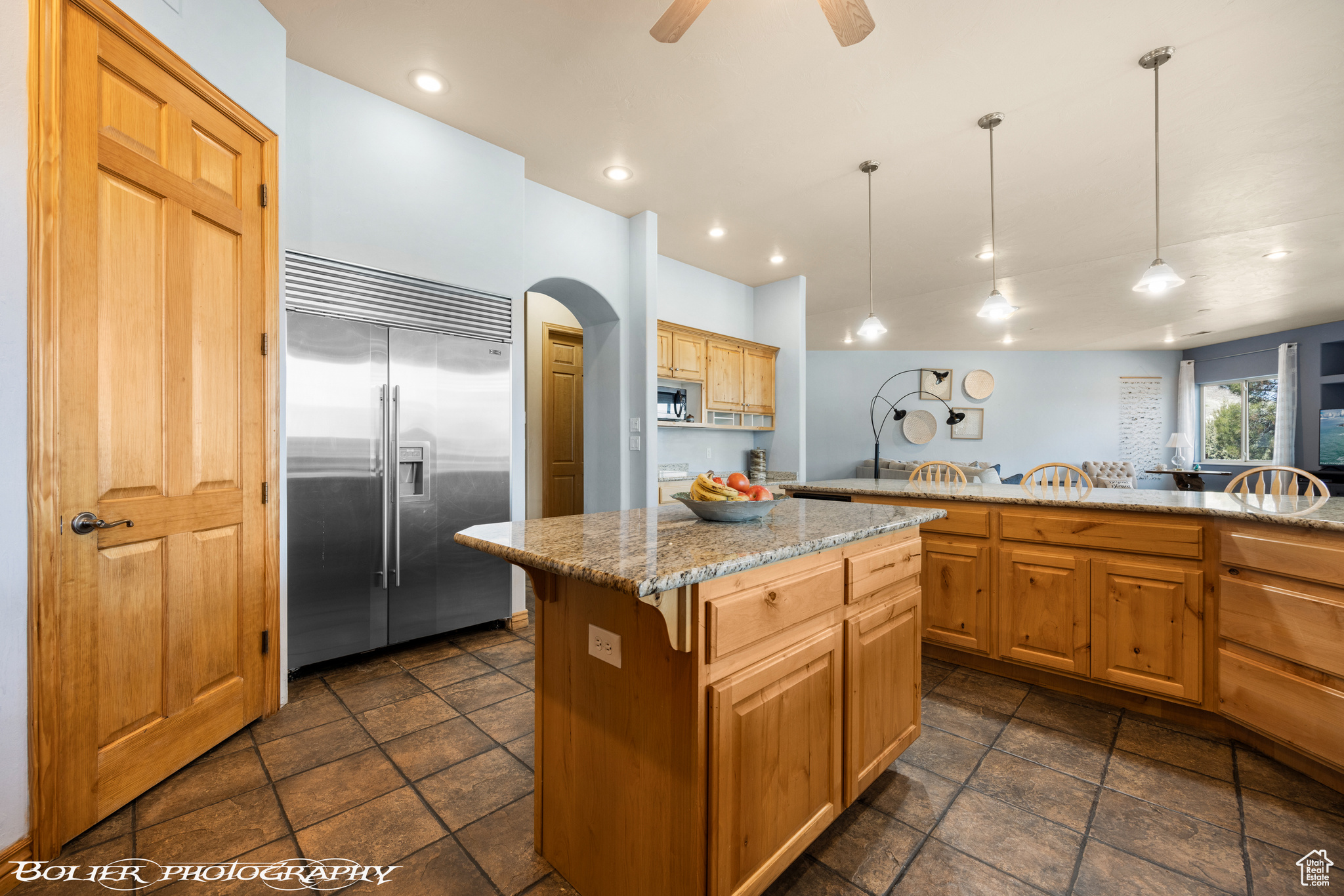 Kitchen with ceiling fan, decorative light fixtures, a center island, light stone counters, and stainless steel appliances