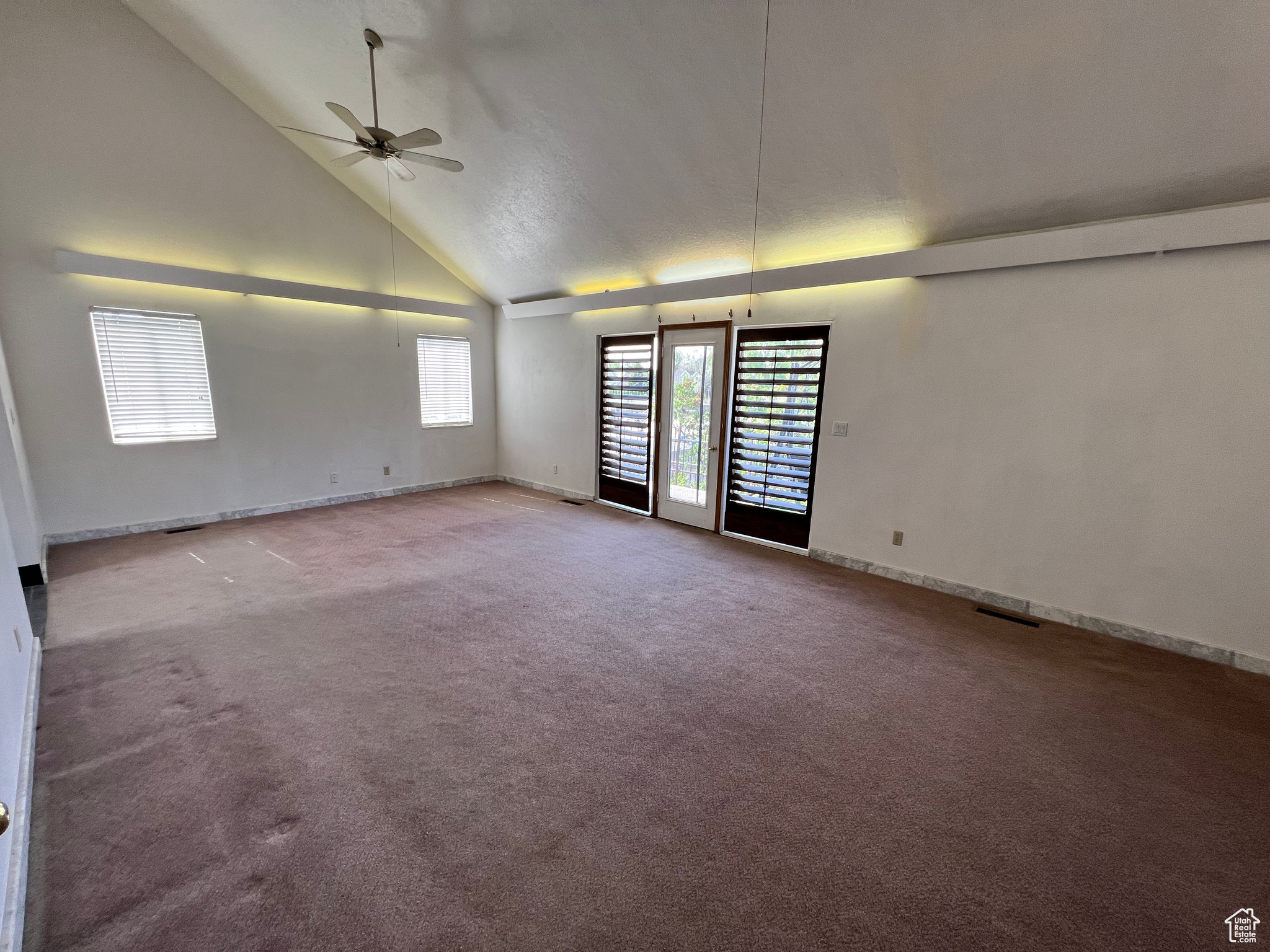 Carpeted empty room with high vaulted ceiling and ceiling fan