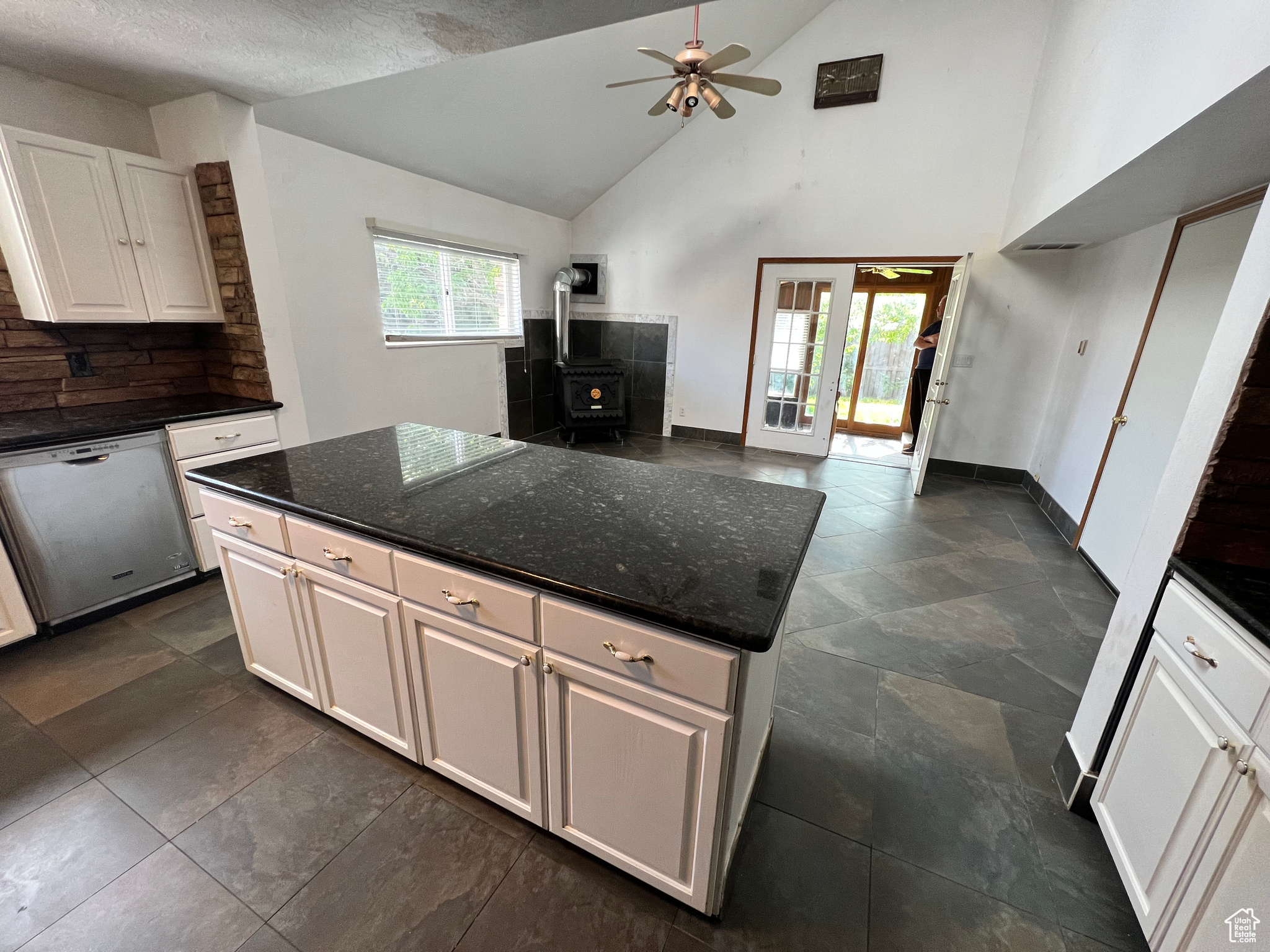 Kitchen with ceiling fan, a wood stove, white dishwasher, and white cabinets