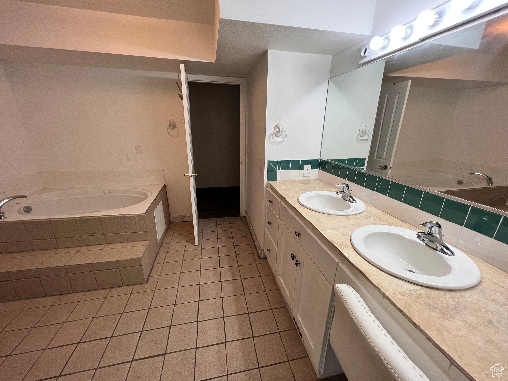 Bathroom featuring tile flooring, double sink, tiled tub, and vanity with extensive cabinet space