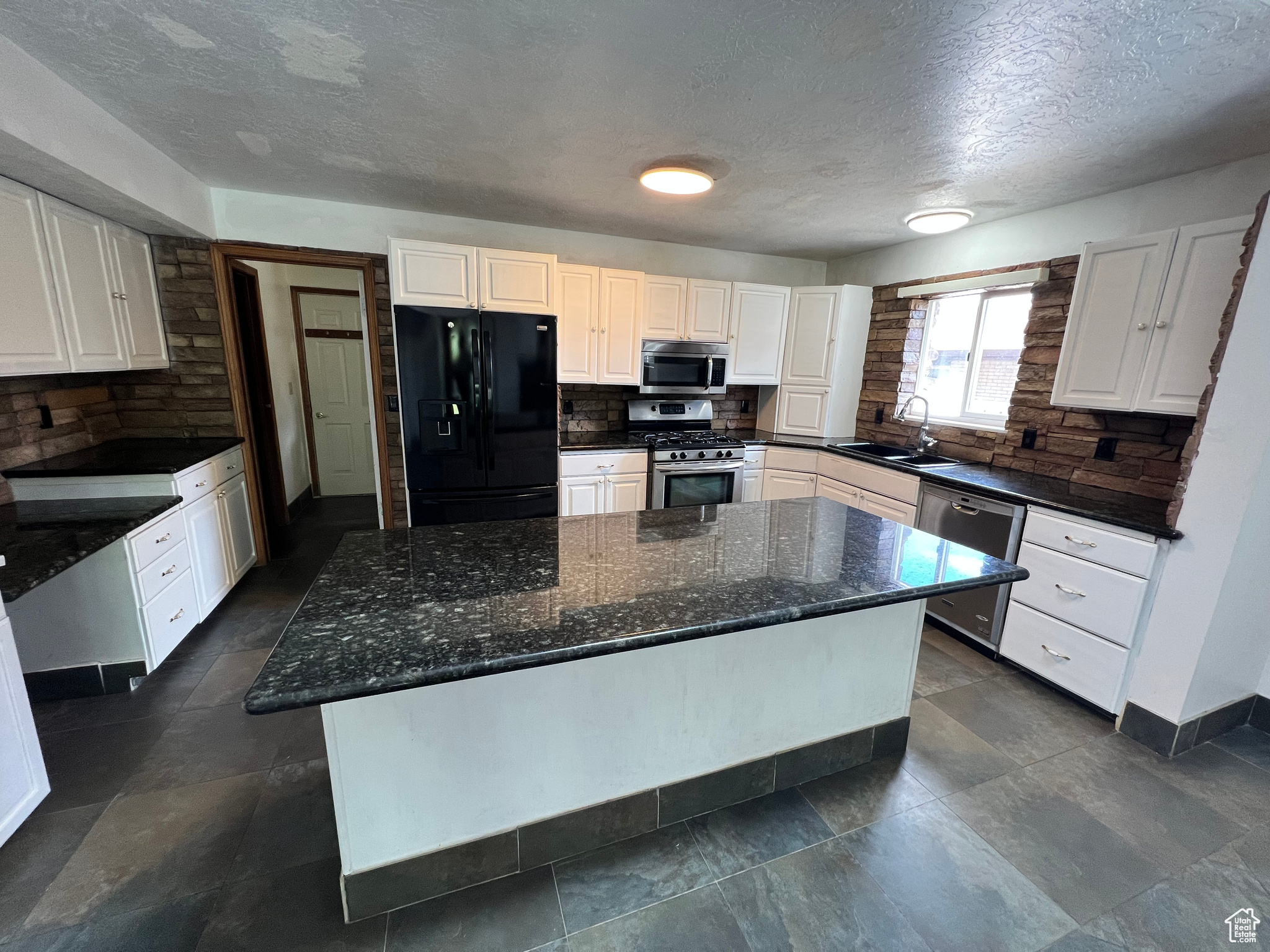 Kitchen featuring white cabinetry, sink, stainless steel appliances, dark stone countertops, and a kitchen island