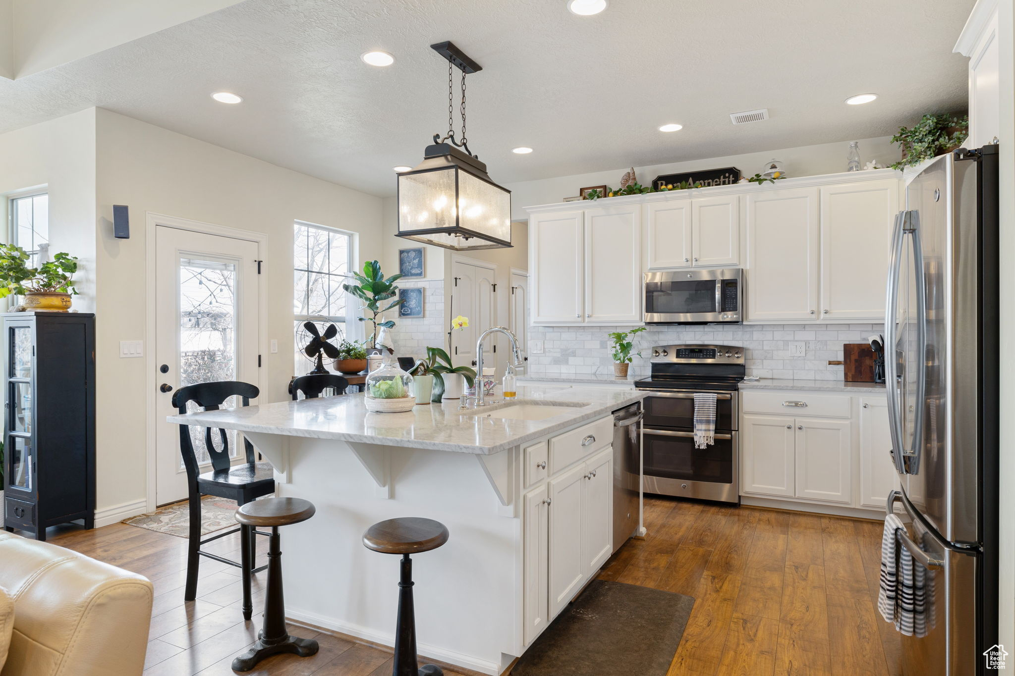 Kitchen featuring pendant lighting, hardwood / wood-style floors, appliances with stainless steel finishes, a kitchen island with sink, and sink