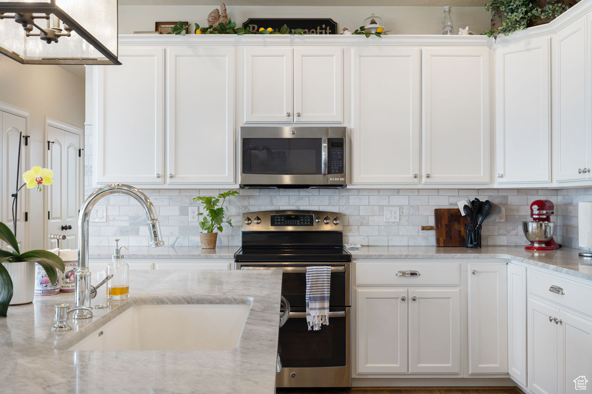 Kitchen featuring white cabinetry, backsplash, appliances with stainless steel finishes, sink, and light stone counters