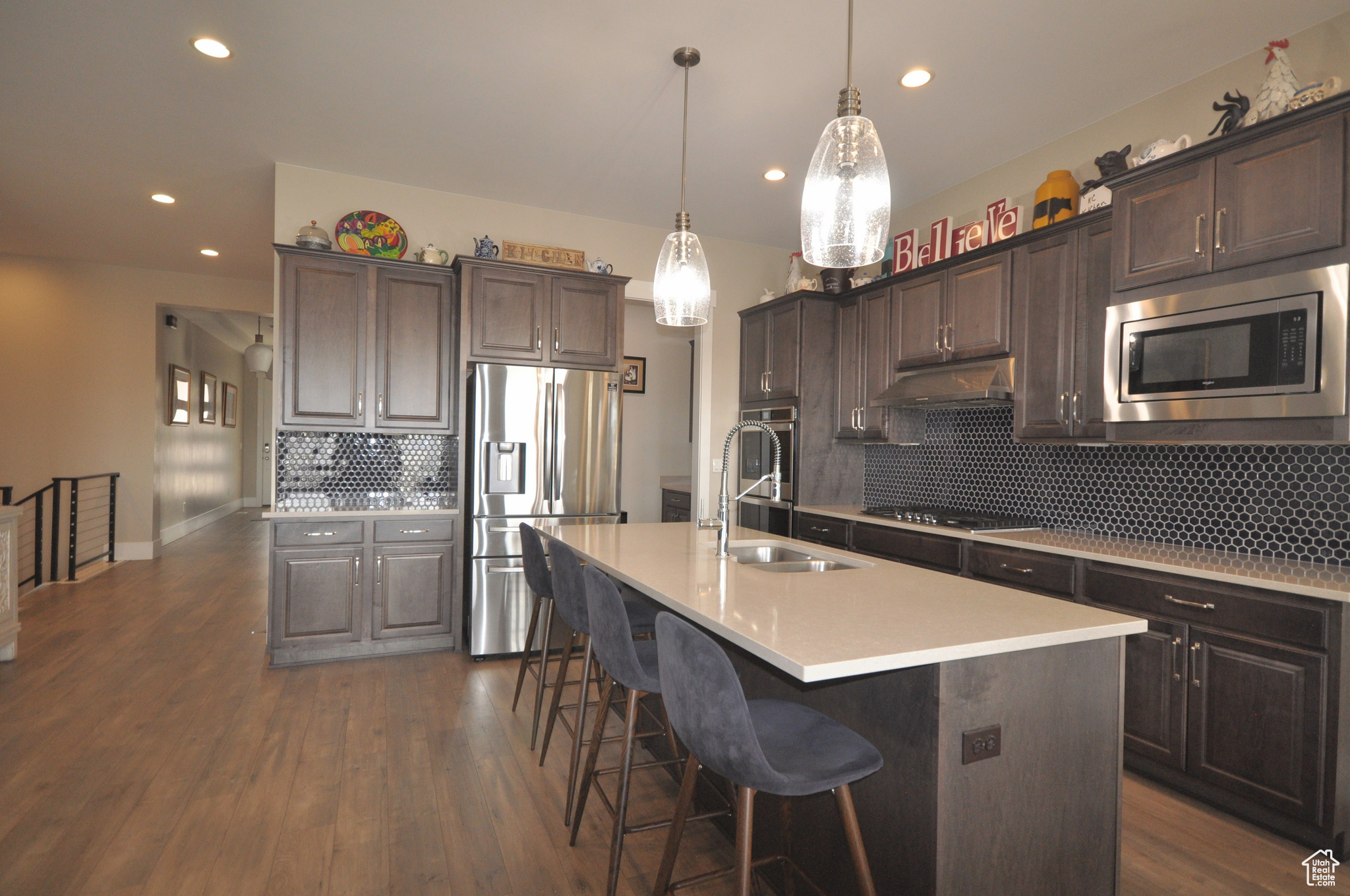Kitchen with tasteful backsplash, appliances with stainless steel finishes, pendant lighting, dark hardwood / wood-style flooring, and an island with sink