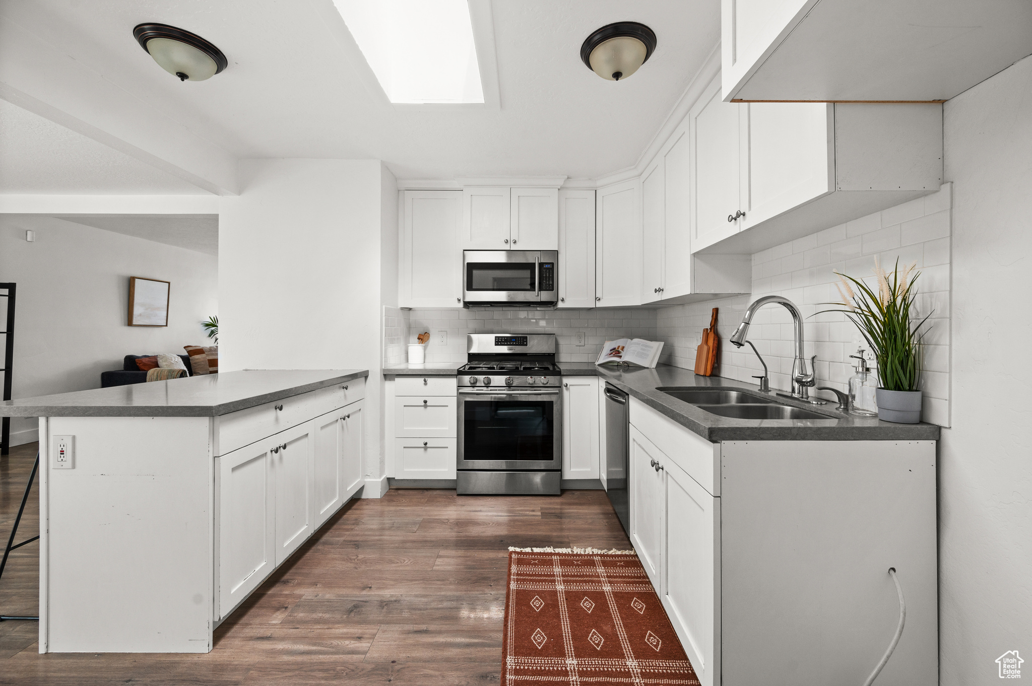 Kitchen with backsplash, appliances with stainless steel finishes, white cabinets, sink, and dark hardwood / wood-style flooring