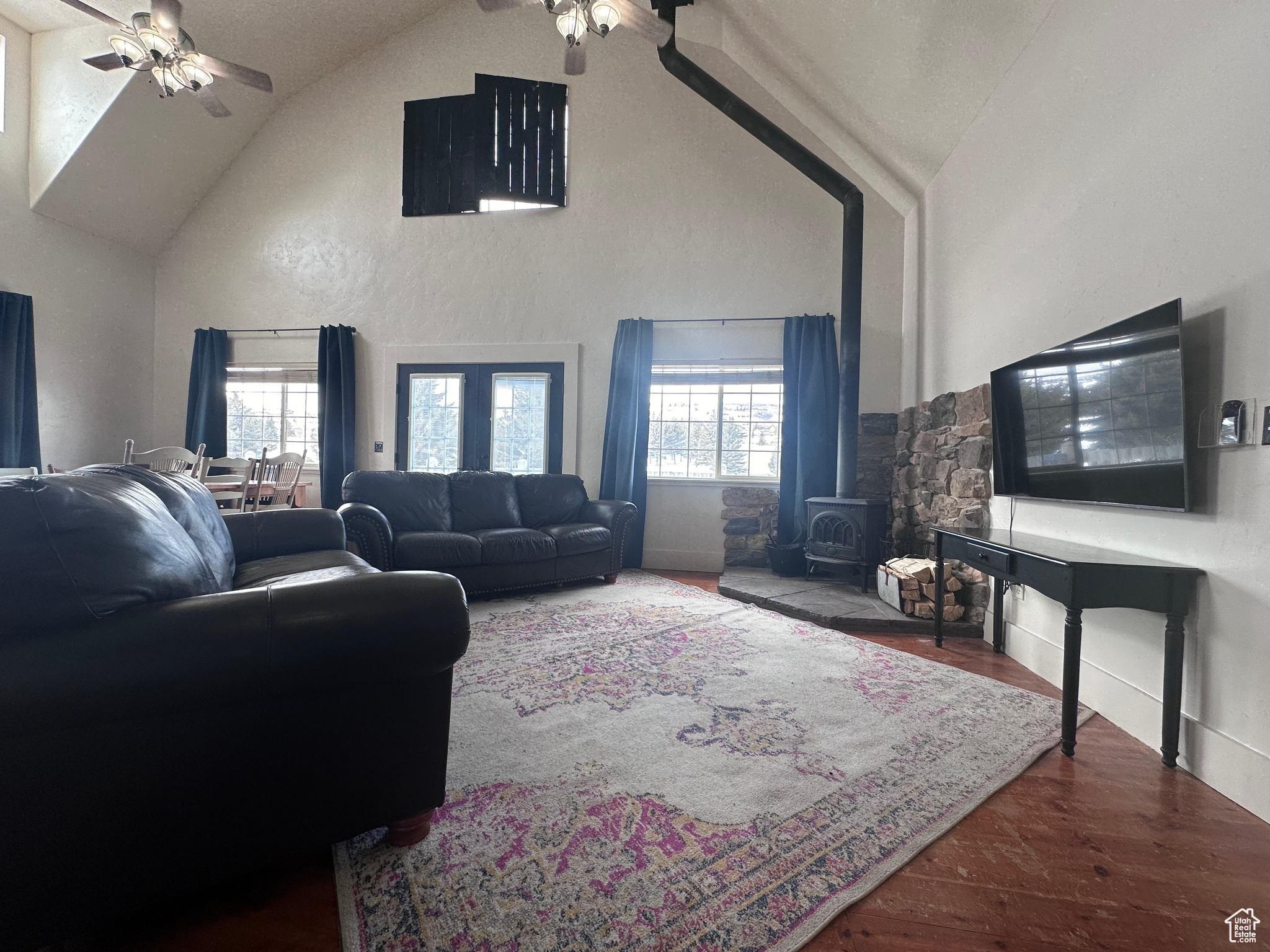 Living room with hardwood floors, a wood stove, plenty of natural light, and ceiling fan
