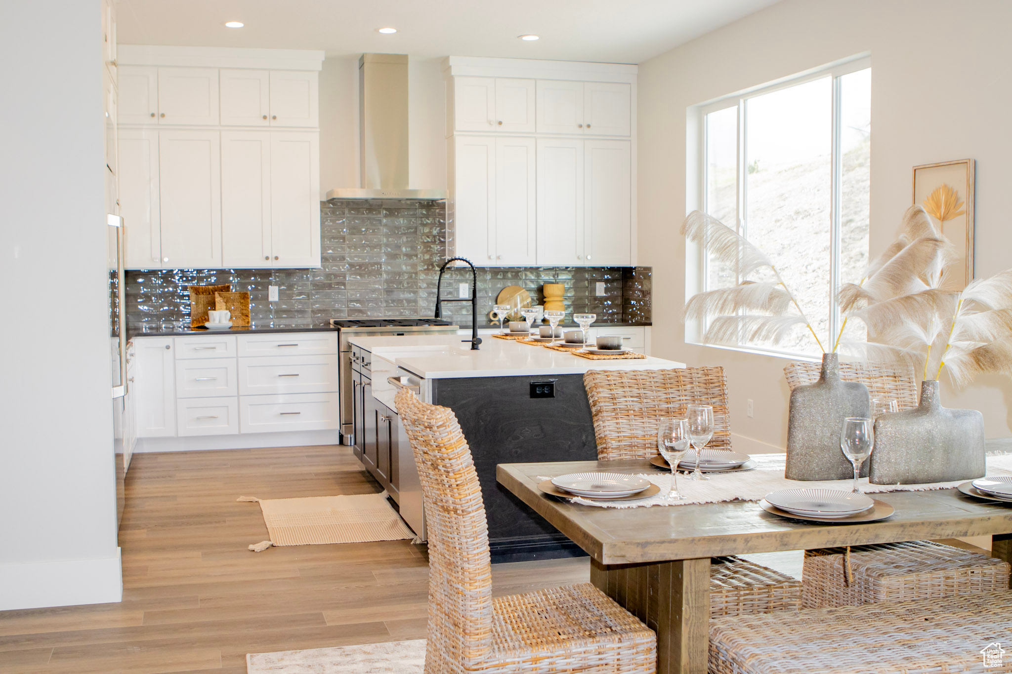 Kitchen with light hardwood / wood-style floors, backsplash, a kitchen island with sink, wall chimney exhaust hood, and white cabinets