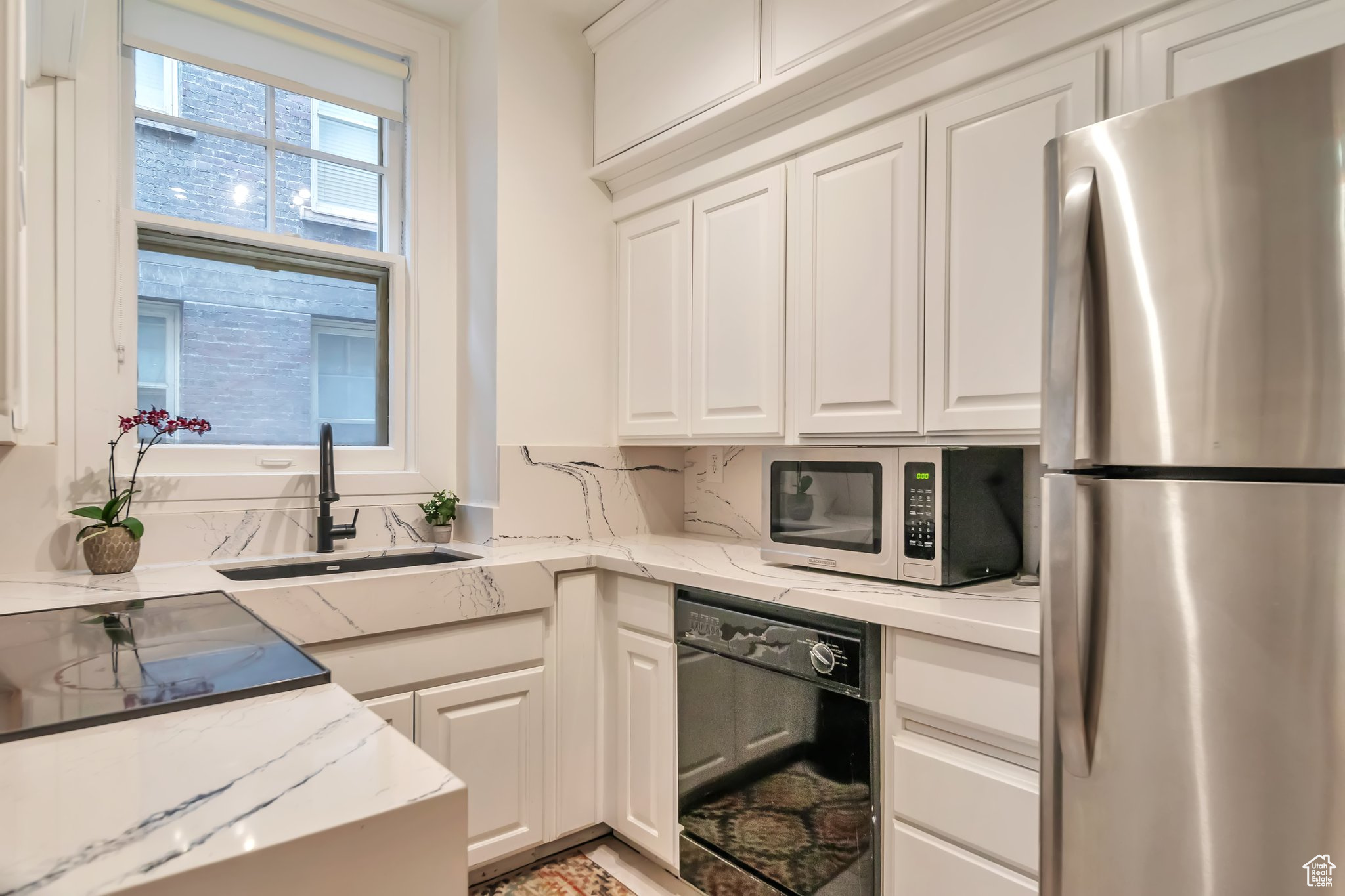 Kitchen with stainless steel fridge, dishwasher, light stone counters, white cabinetry, and sink