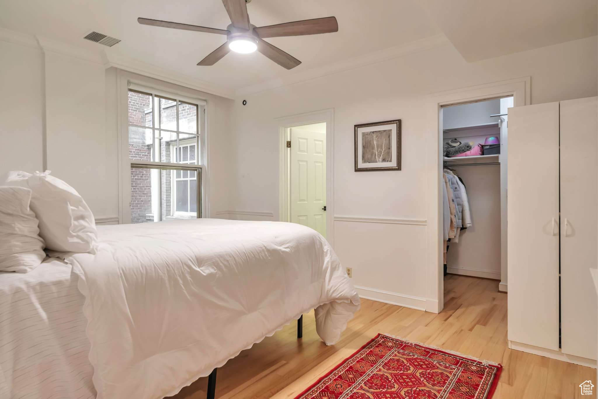 Bedroom featuring ornamental molding, a closet, light wood-type flooring, a walk in closet, and ceiling fan