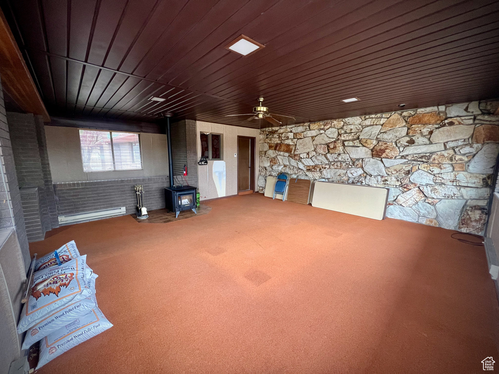 Interior space featuring a wood stove, ceiling fan, wooden ceiling, a baseboard heating unit, and carpet floors