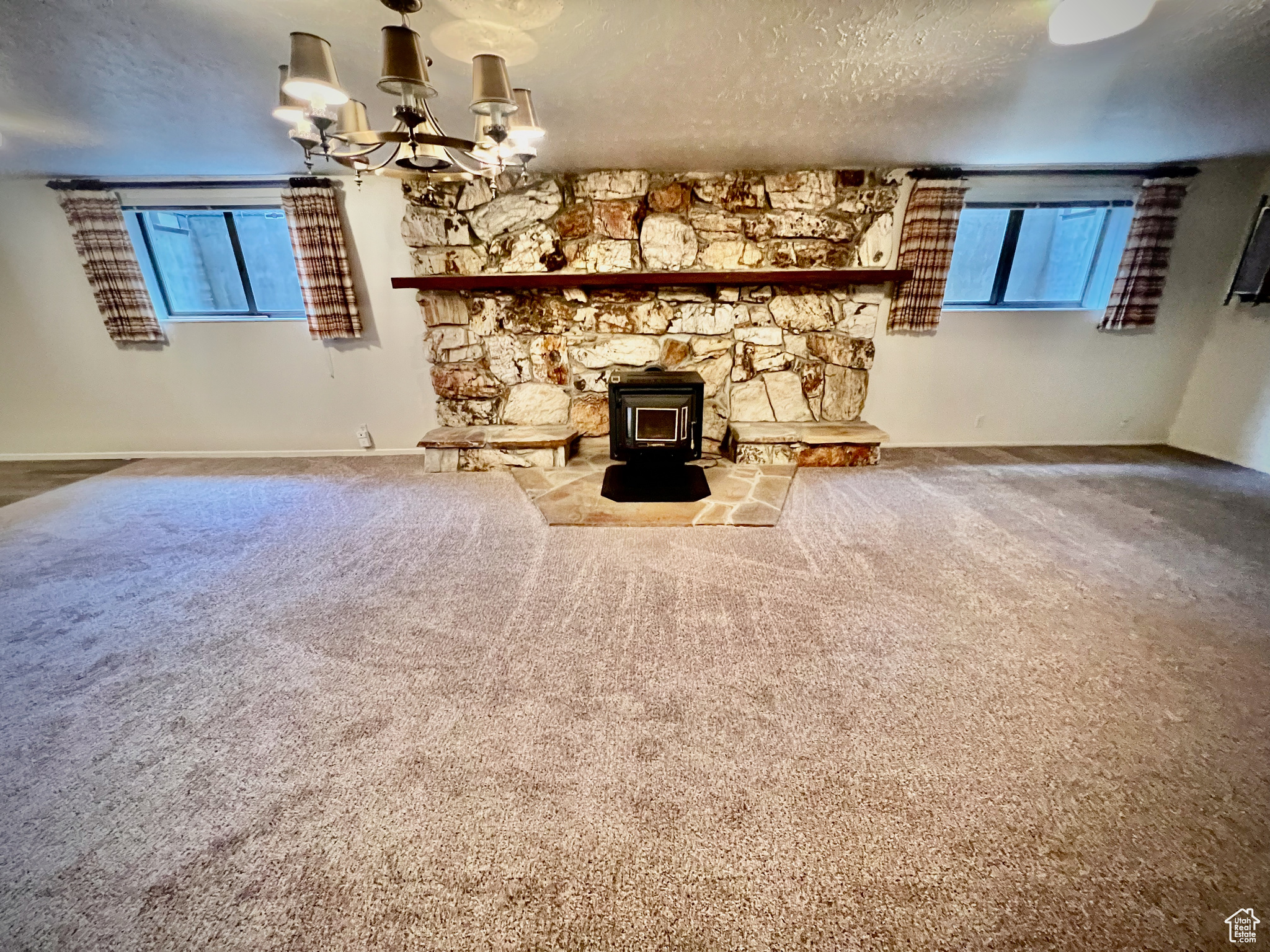 Unfurnished living room featuring carpet flooring, a textured ceiling, a wood stove, and a healthy amount of sunlight