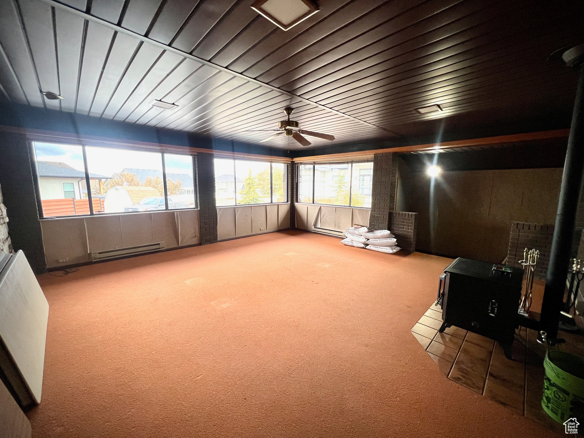 Sunroom with ceiling fan, a wood stove, and a baseboard heating unit